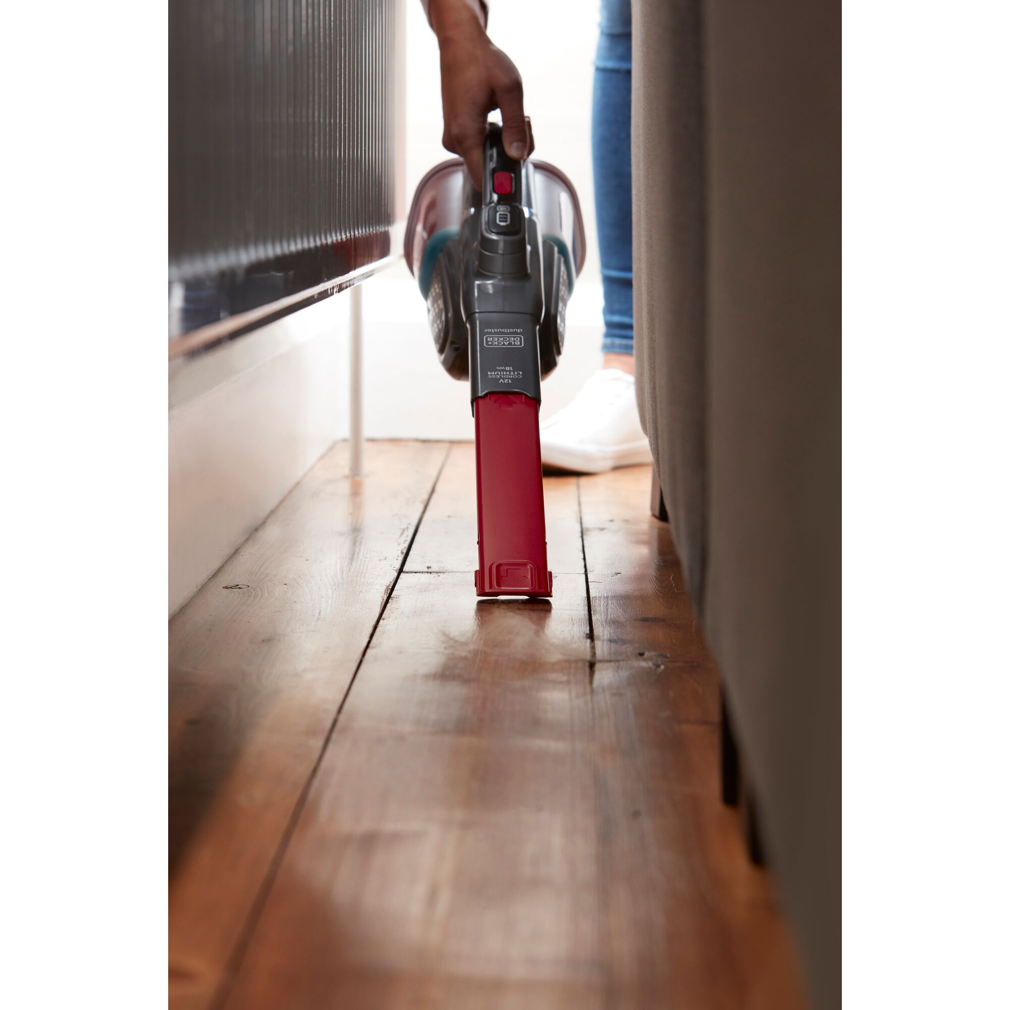 BLACKDECKER BHHV315J handheld vacuum cleaning narrow space beside furniture on wooden floor.