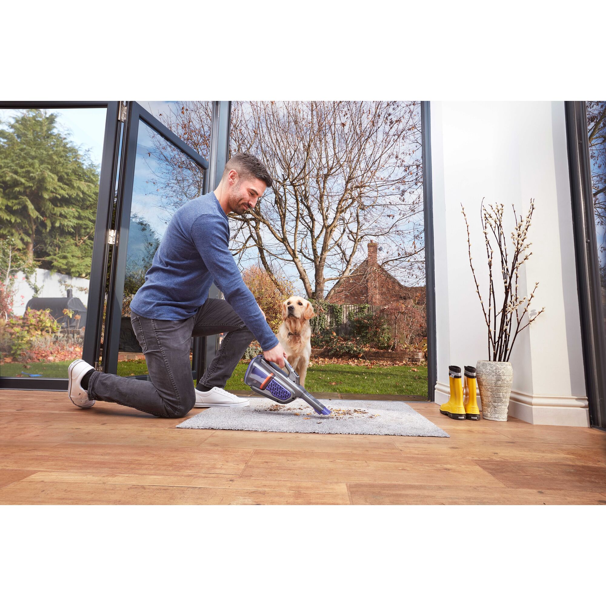 BLACKDECKER BHHV520BFP07 handheld vacuum cleaning dirt from rug near open door with dog outside.