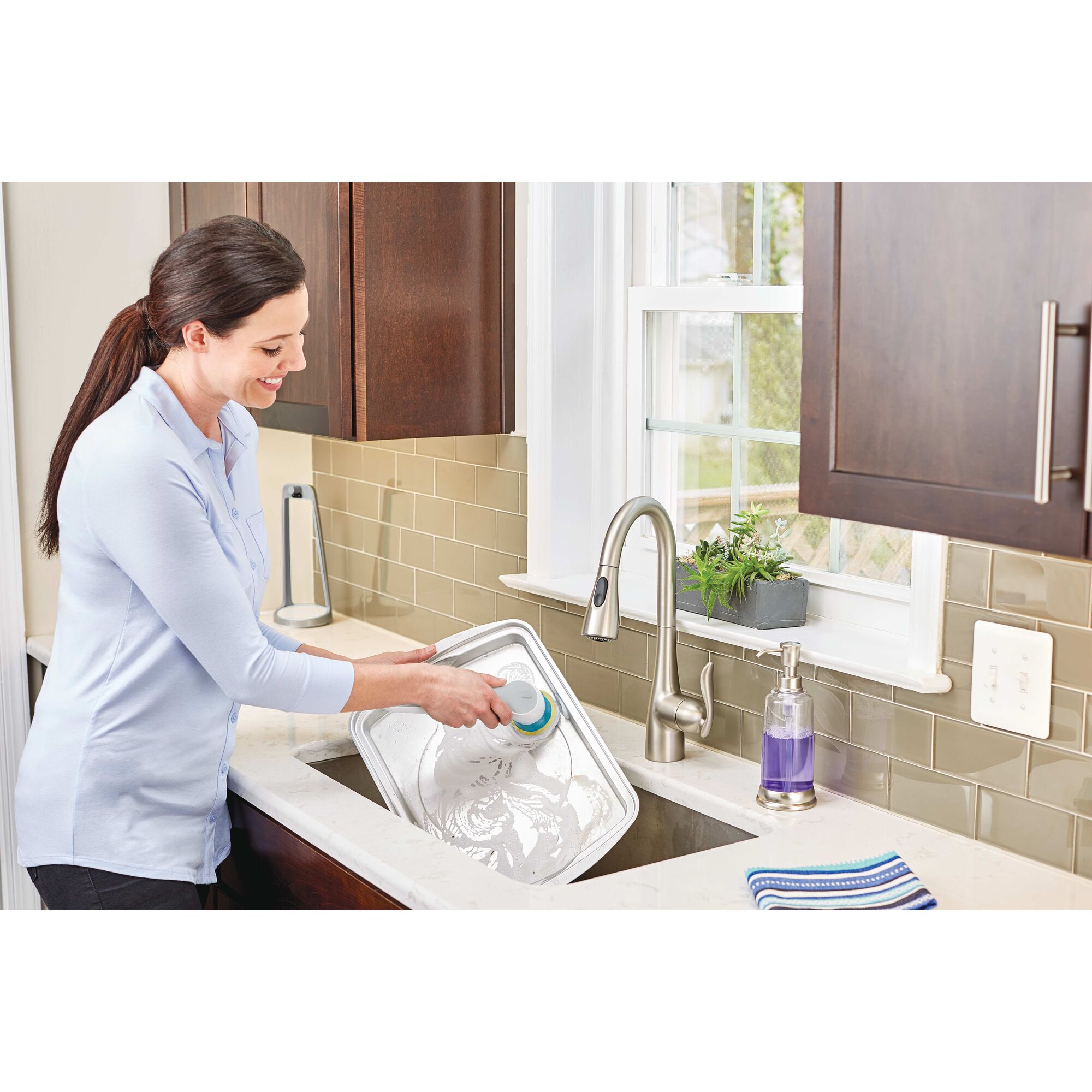 Grimebuster Pro Rechargeable Powered Scrubber being used by person to wash steel tray in kitchen.