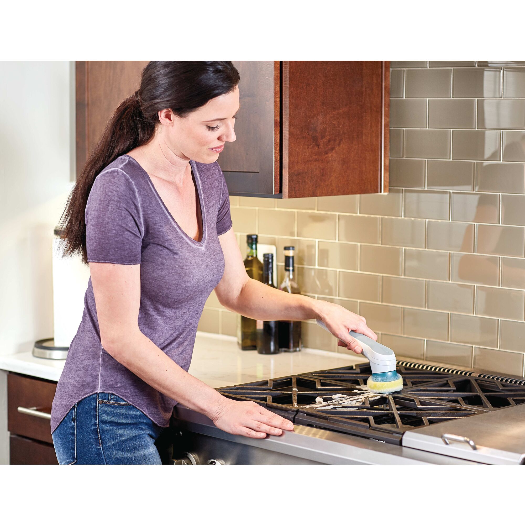 Grimebuster Pro Rechargeable Powered Scrubber with Charging Stand being used to clean stove tops by a person.