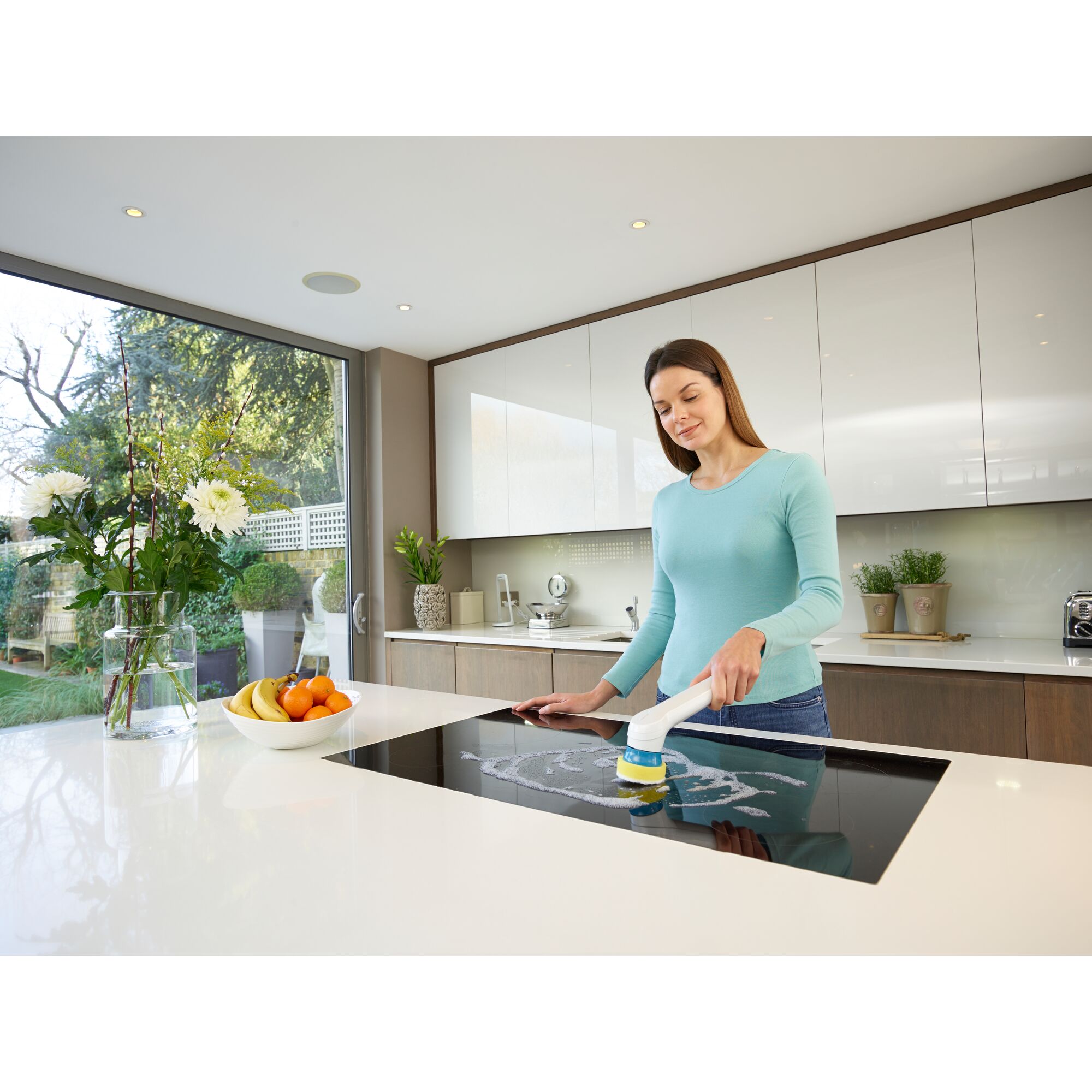 BLACKDECKER BHPC110 hand scrubber cleaning a kitchen stovetop, modern kitchen setting, fruit bowl, plants visible.