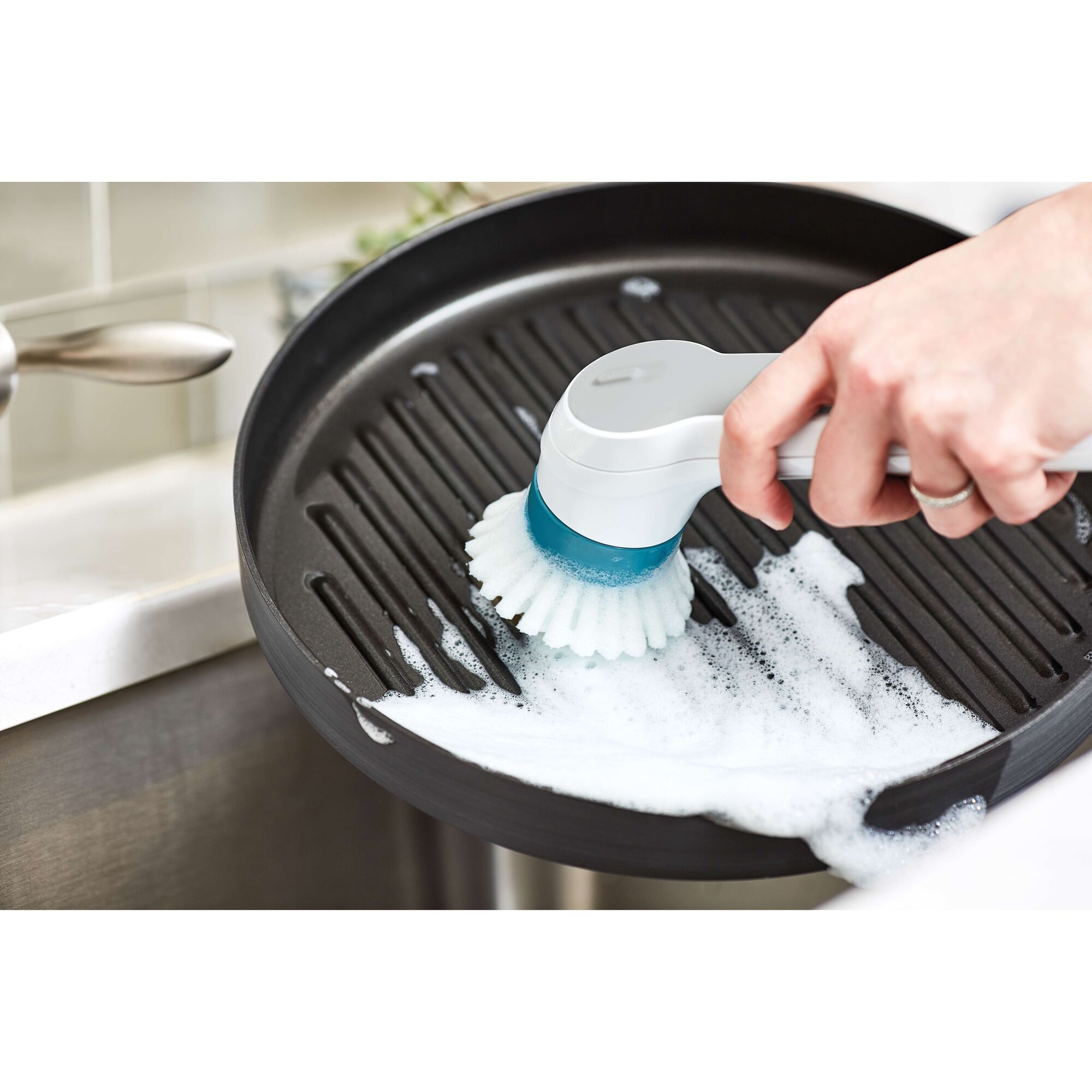 BLACKDECKER BHPC110 cleaning brush scrubs a soapy grill pan, handheld kitchen tool in use.