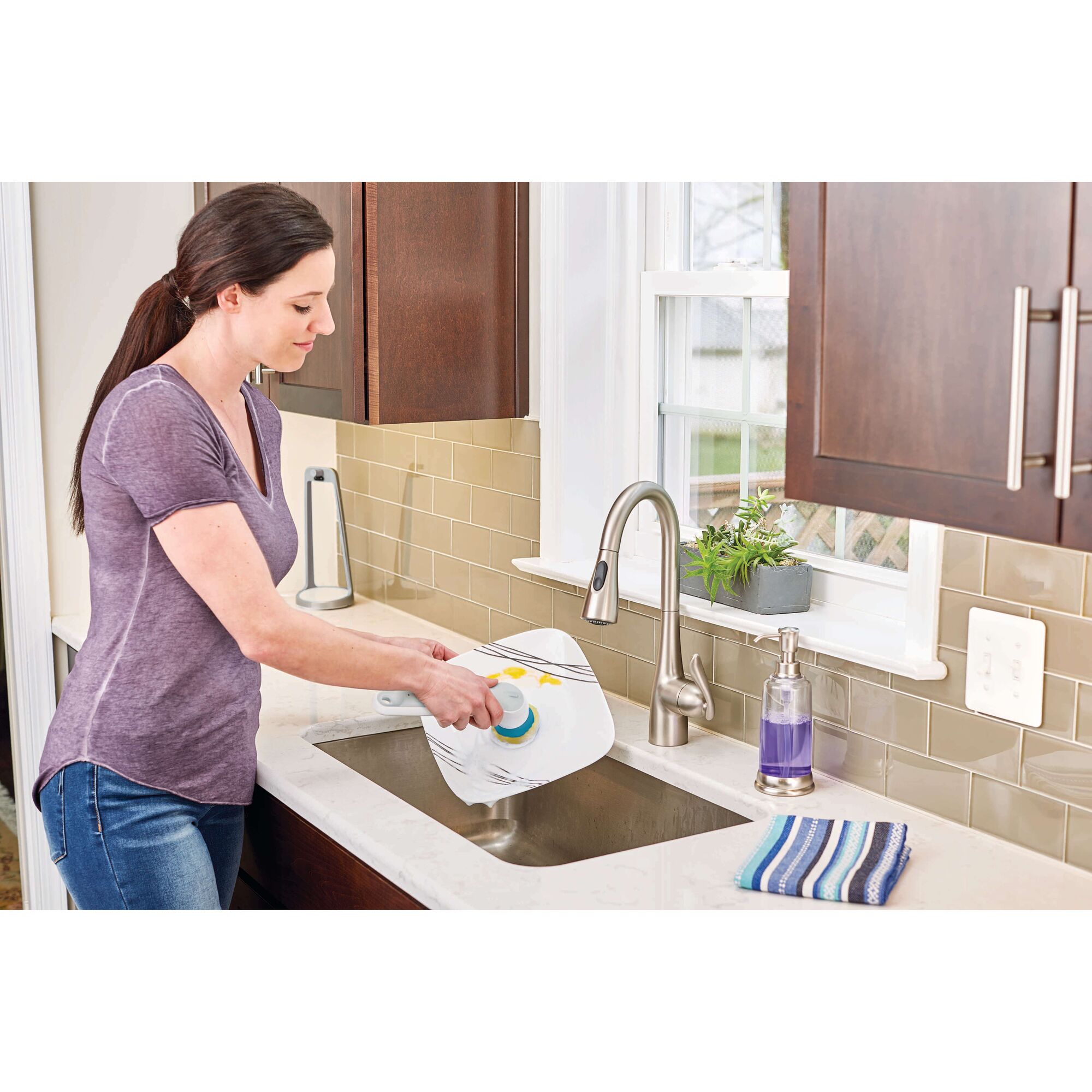 BLACKDECKER BHPC110 handheld scrub brush cleaning a plate at a kitchen sink.