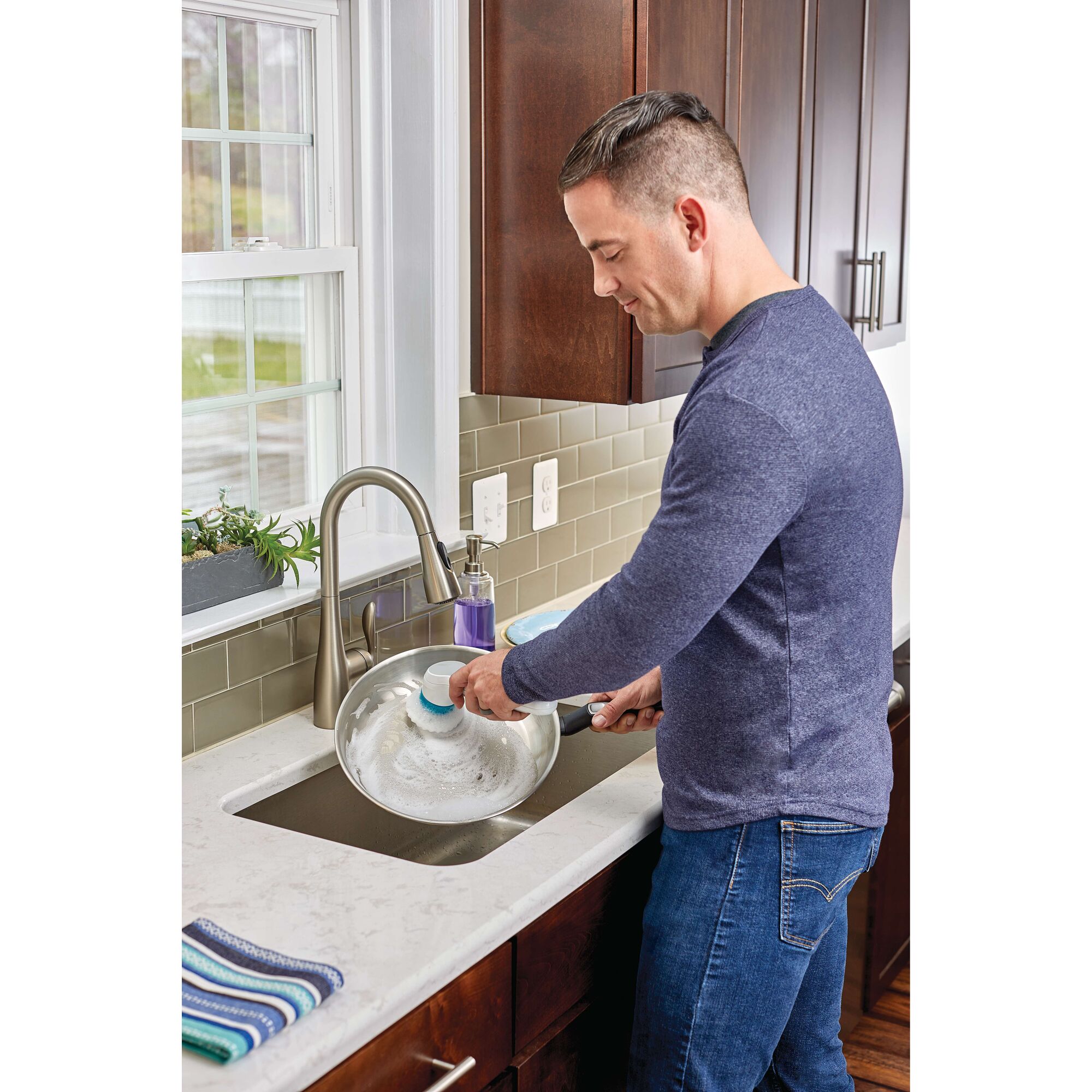 BLACKDECKER BHPC110 handheld scrub brush cleaning a frying pan in a kitchen sink.