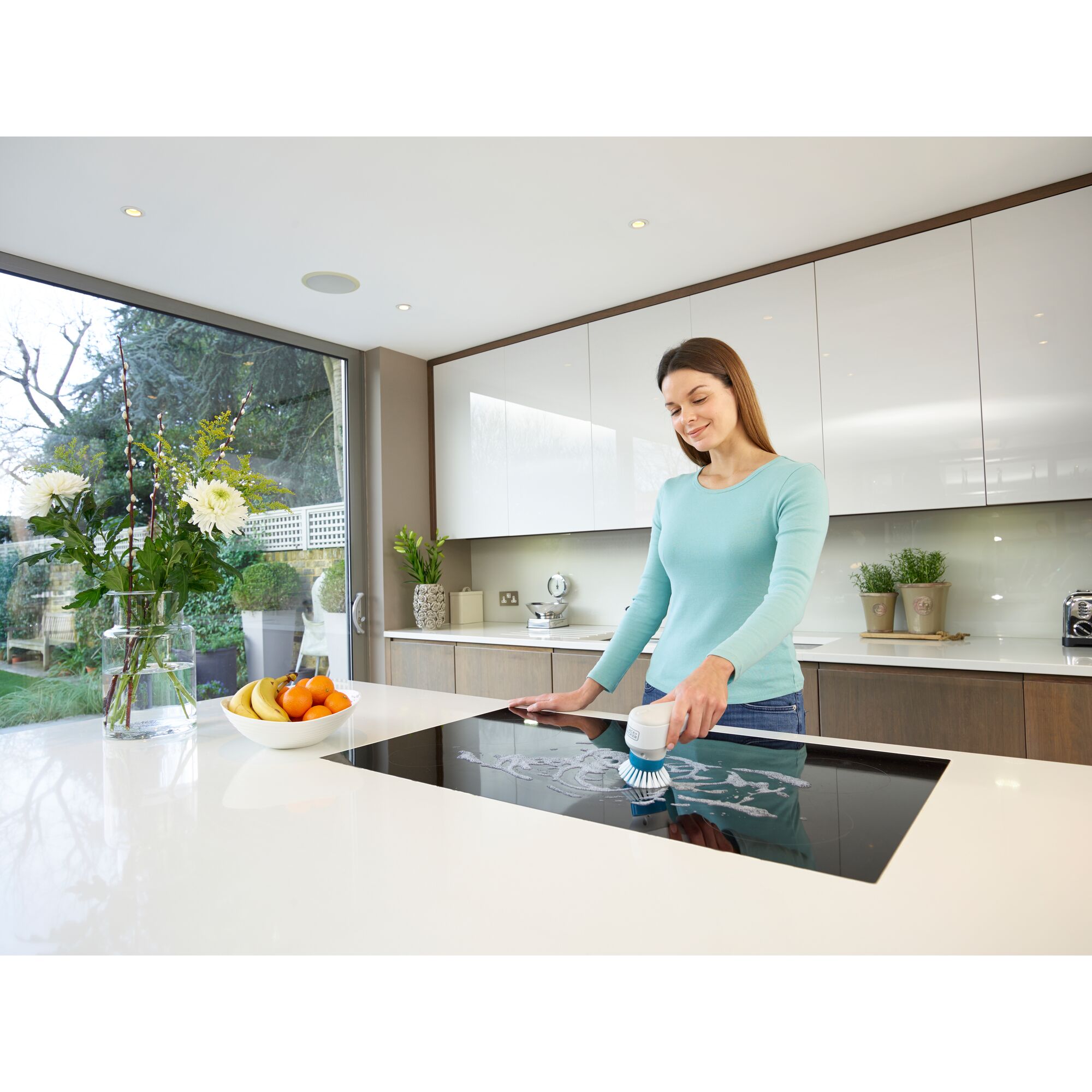 BLACKDECKER BHPC130 handheld scrubber cleaning stovetop in modern kitchen, fruit bowl and flowers nearby.