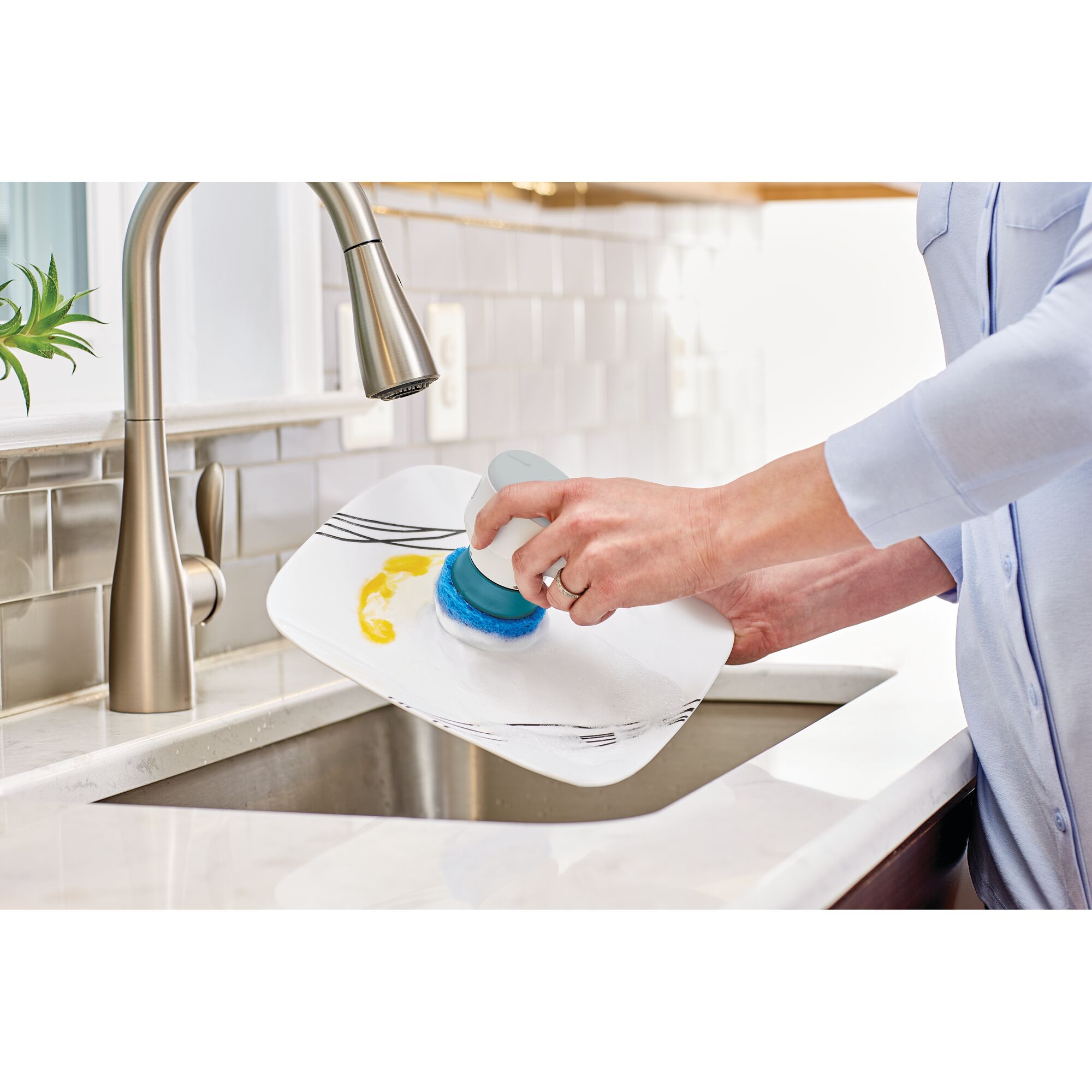 BLACKDECKER BHPC130 handheld scrub brush cleaning a plate at a kitchen sink, photography side angle.