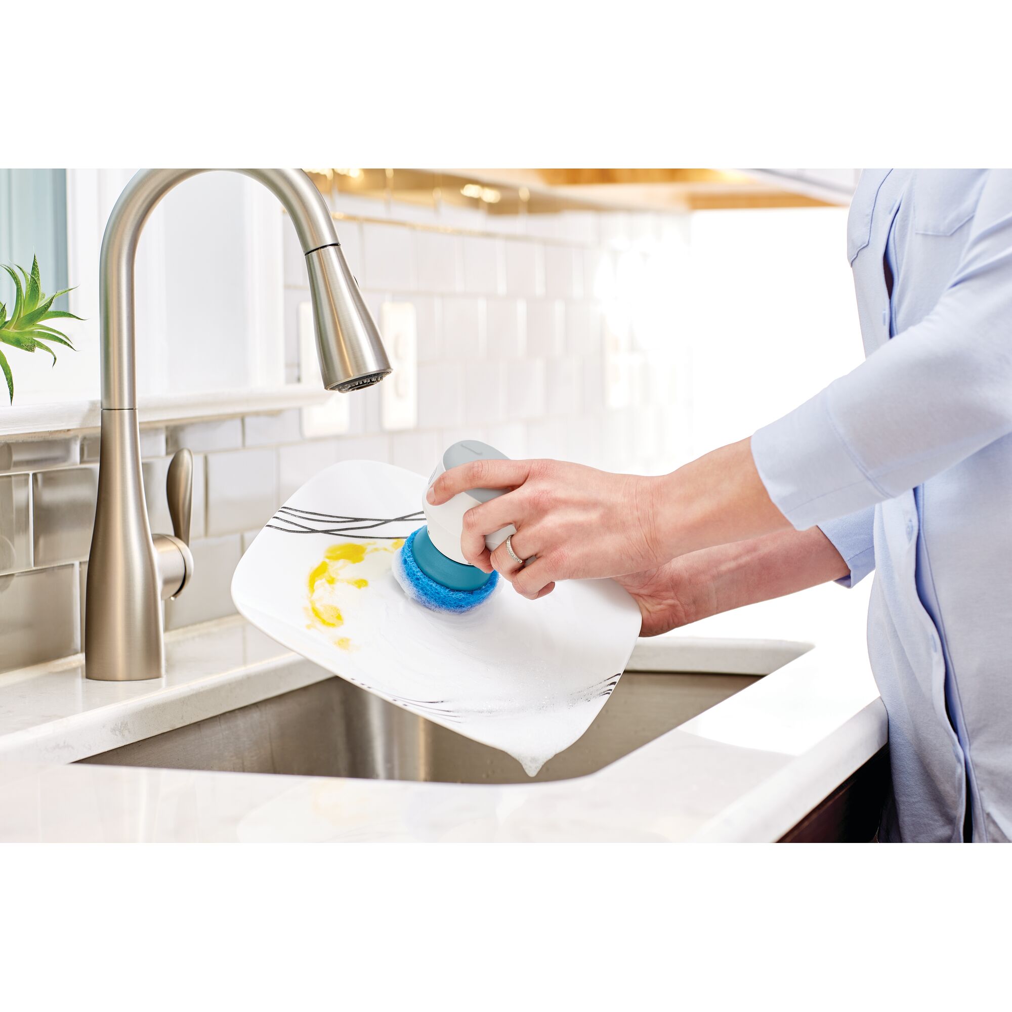 BLACKDECKER BHPC130 handheld scrubber cleaning a plate with soap in a kitchen sink, side angle.