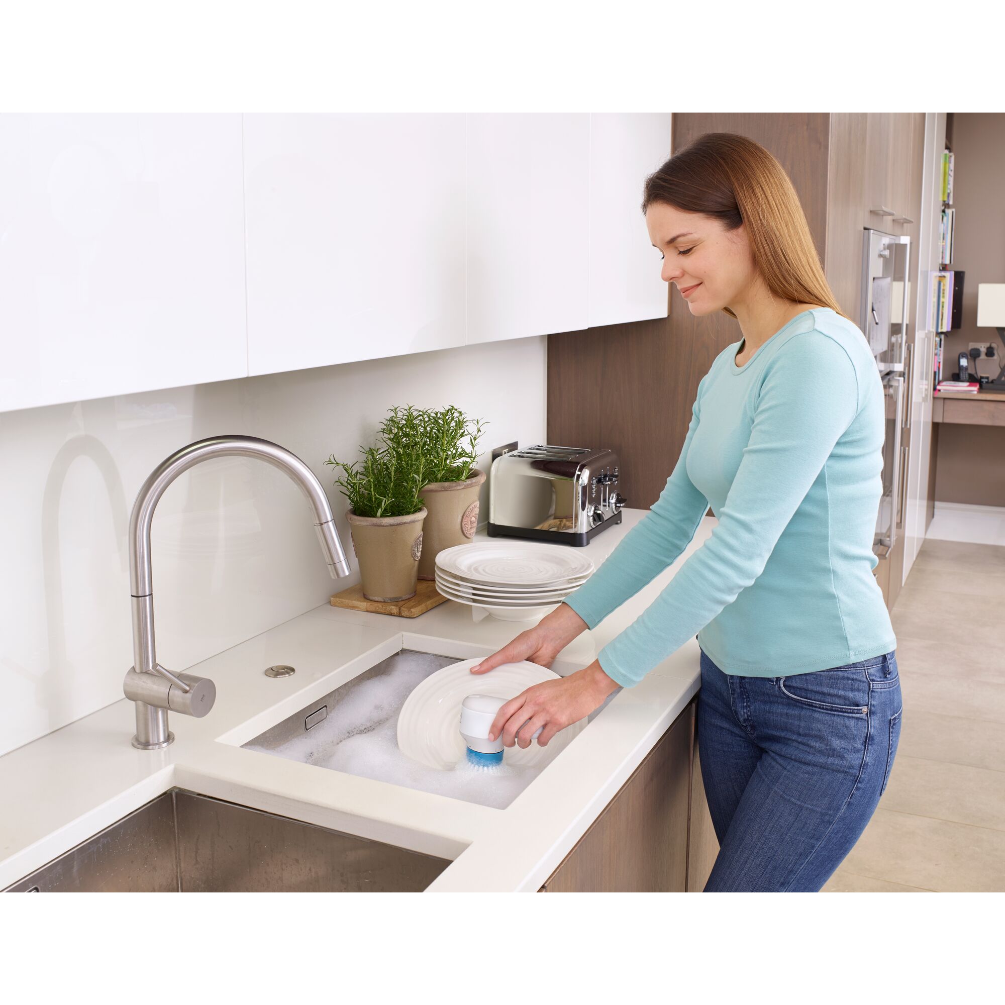 BLACKDECKER BHPC130 handheld dish scrubber in use cleaning plates at a kitchen sink.