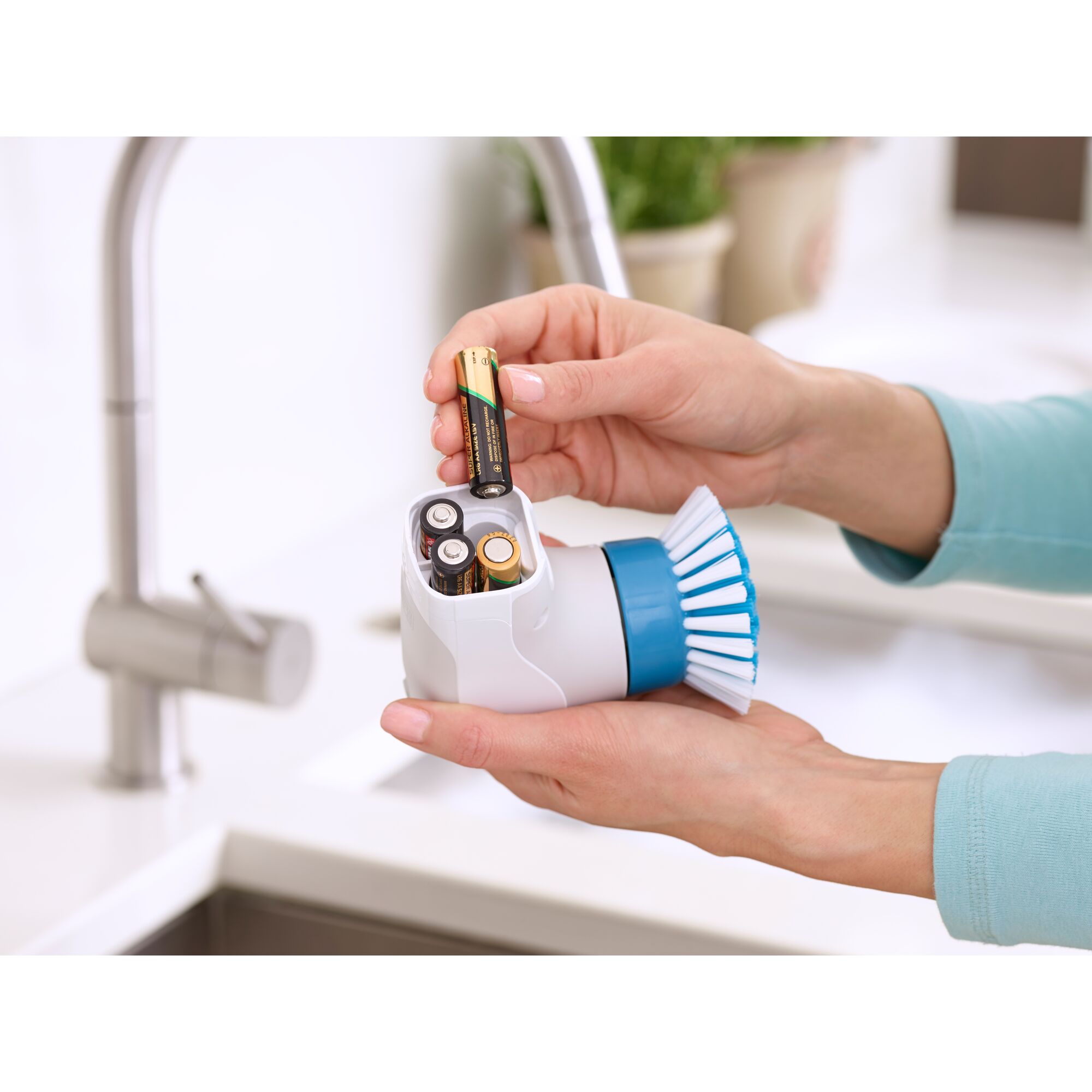 BLACKDECKER BHPC130 handheld scrub brush with blue bristles, batteries being inserted, kitchen setting.
