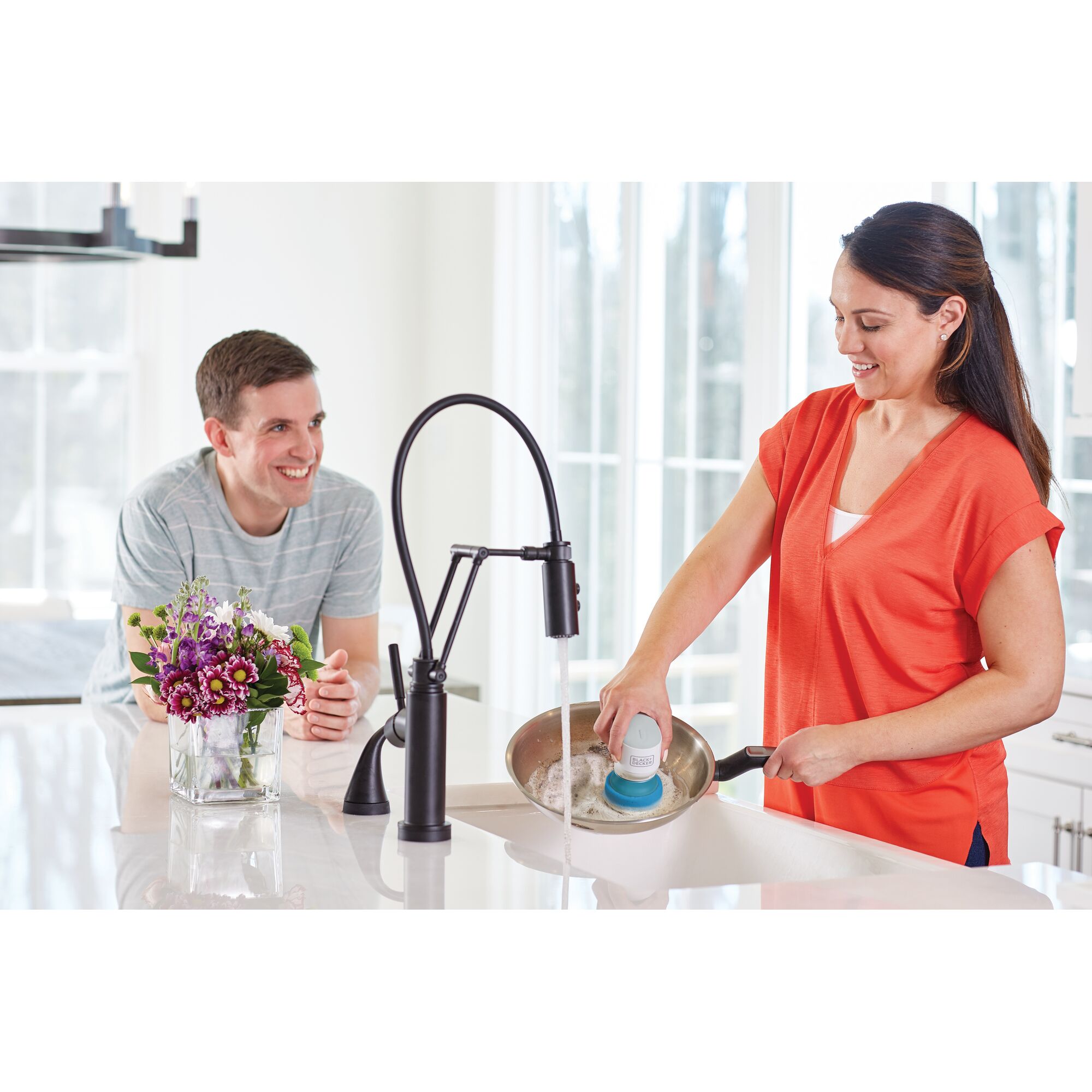 BLACK+DECKER BHPC130 kitchen scrubber used to clean a frying pan under faucet in a bright kitchen setting.