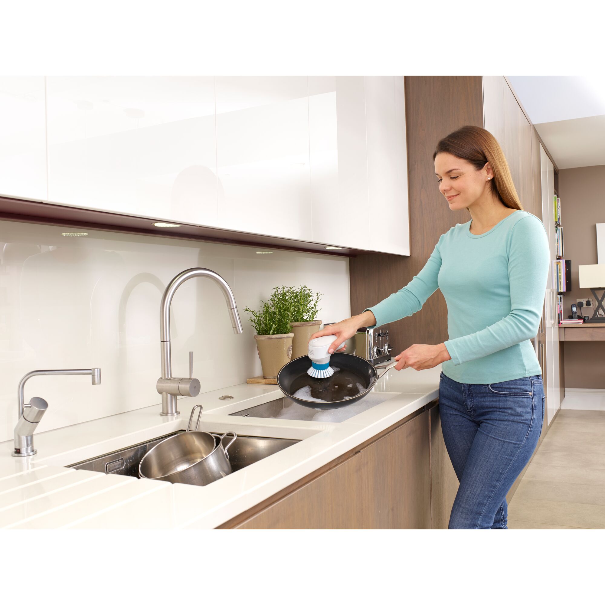 BLACKDECKER BHPC130 handheld scrubber used to clean a frying pan in a modern kitchen.