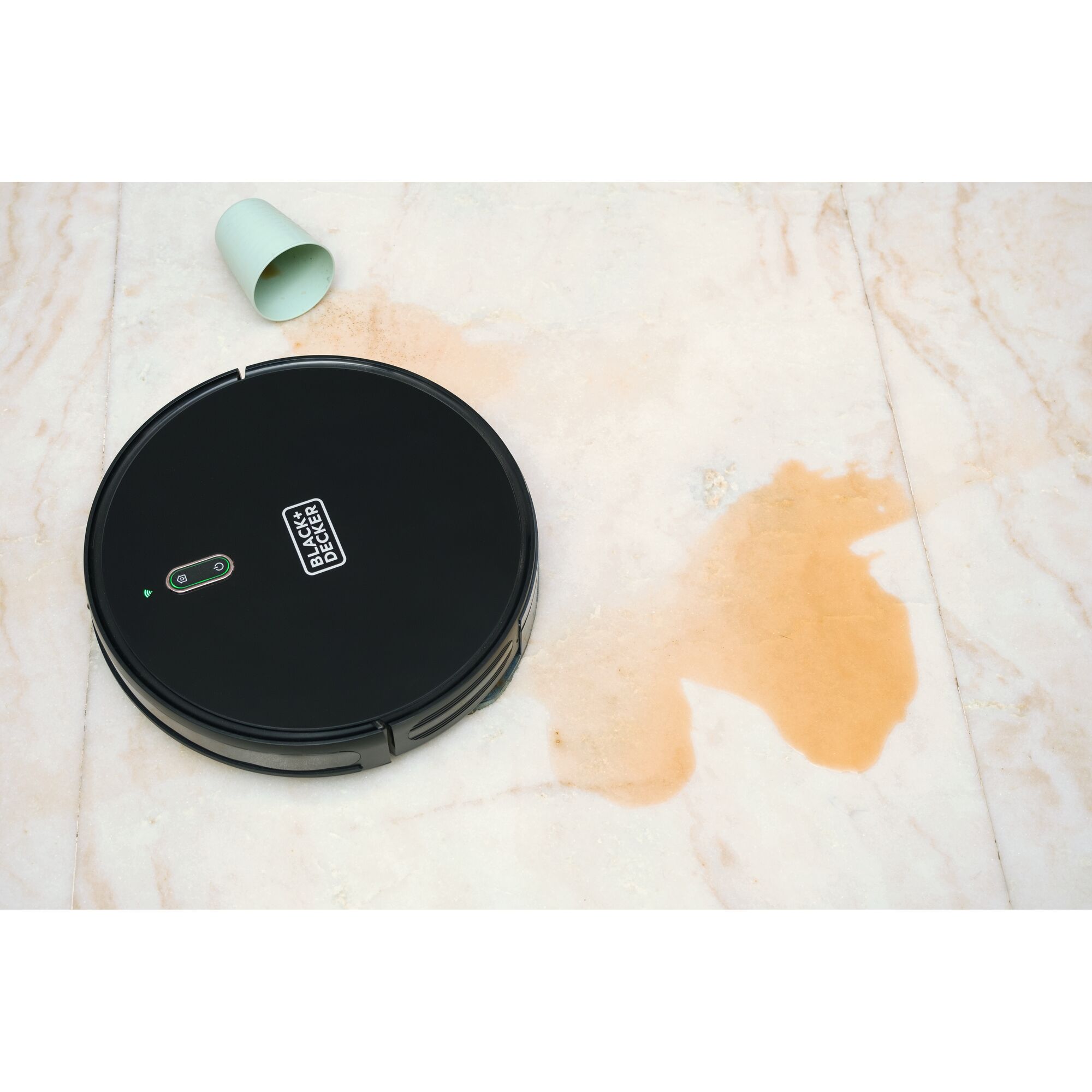 BLACKDECKER BRVA425B00 robotic vacuum on marble floor near spilled liquid and green cup, top view.