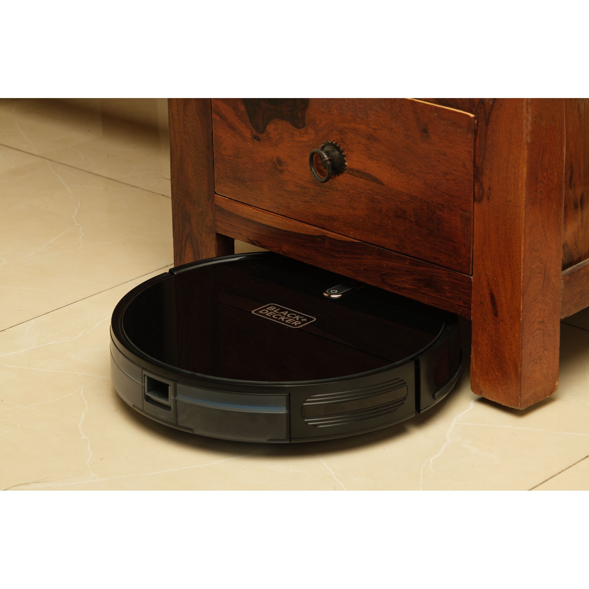 BLACK+DECKER BRVA425B00 robot vacuum cleaning under wooden furniture on beige tile floor.
