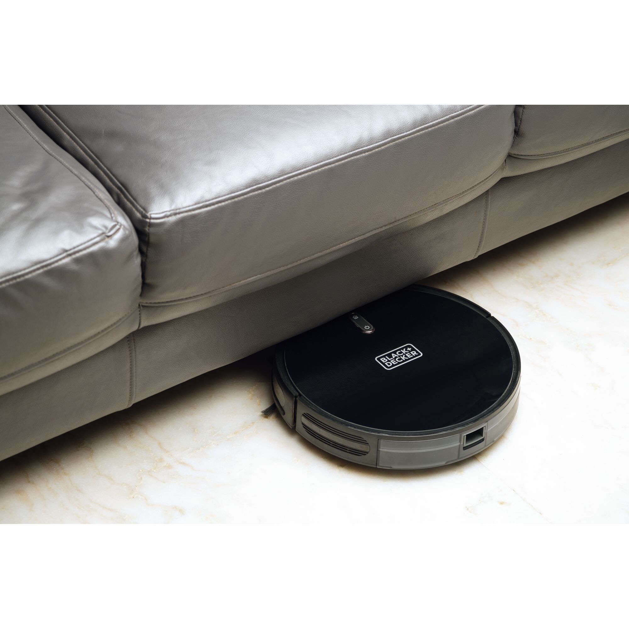 BLACKDECKER BRVA425B00 robotic vacuum cleaner cleaning under a gray sofa on marble flooring.