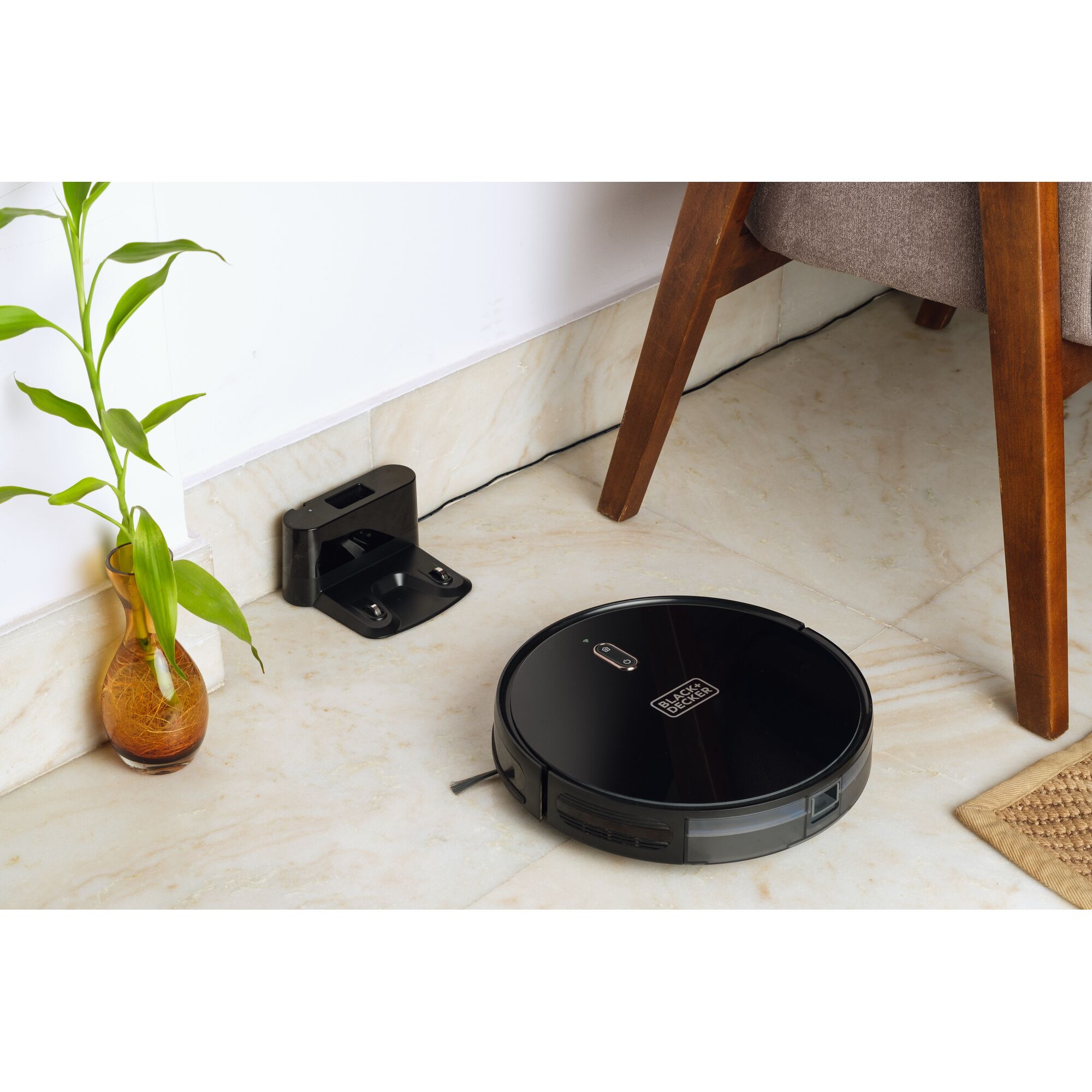 BLACKDECKER BRVA425B00 robot vacuum cleaner on tile floor near charging station and wooden chair.