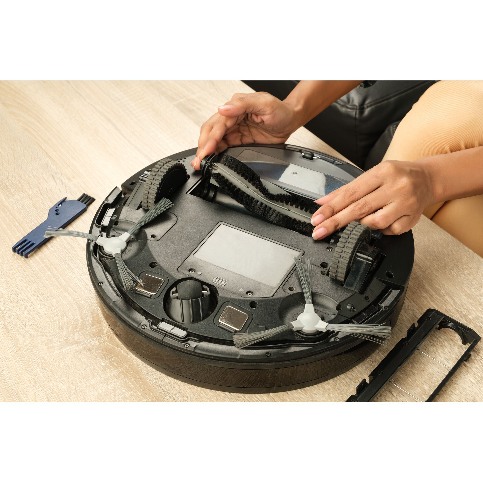 BLACKDECKER BRVA425B00 robot vacuum with exposed bottom showing maintenance and brush removal on wooden table.