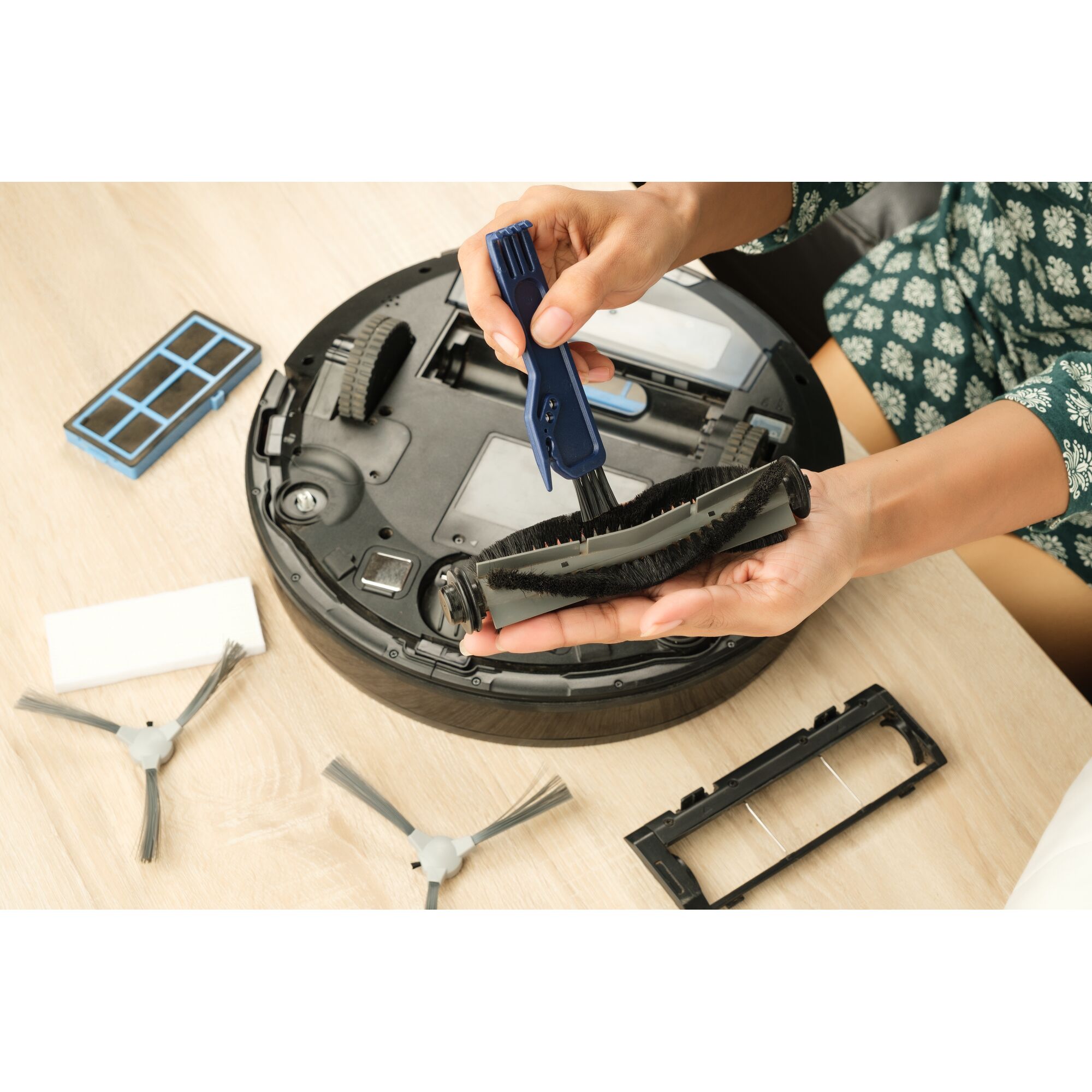 BLACKDECKER BRVA425B00 robotic vacuum brush being cleaned with a tool, spare parts on wooden table.