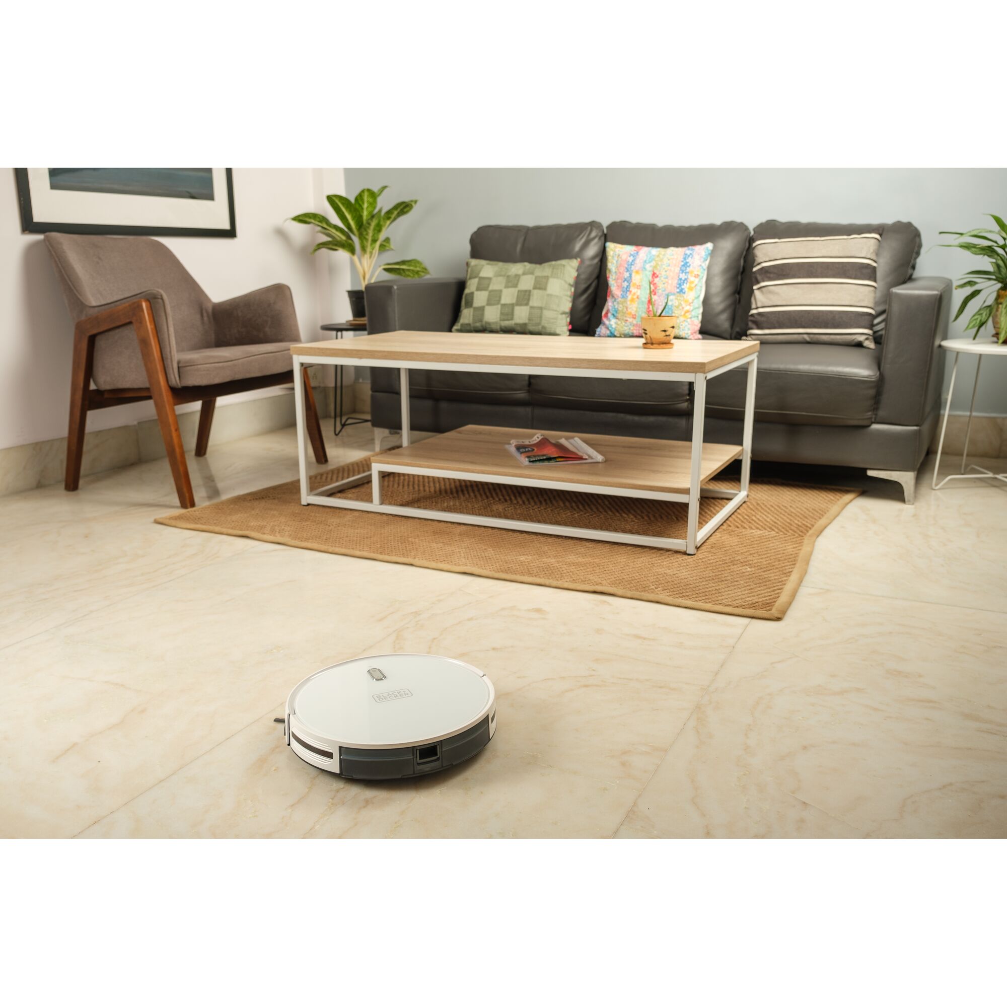 BLACKDECKER BRVA425B10 robot vacuum in a living room setting with sofa, coffee table, and chair.