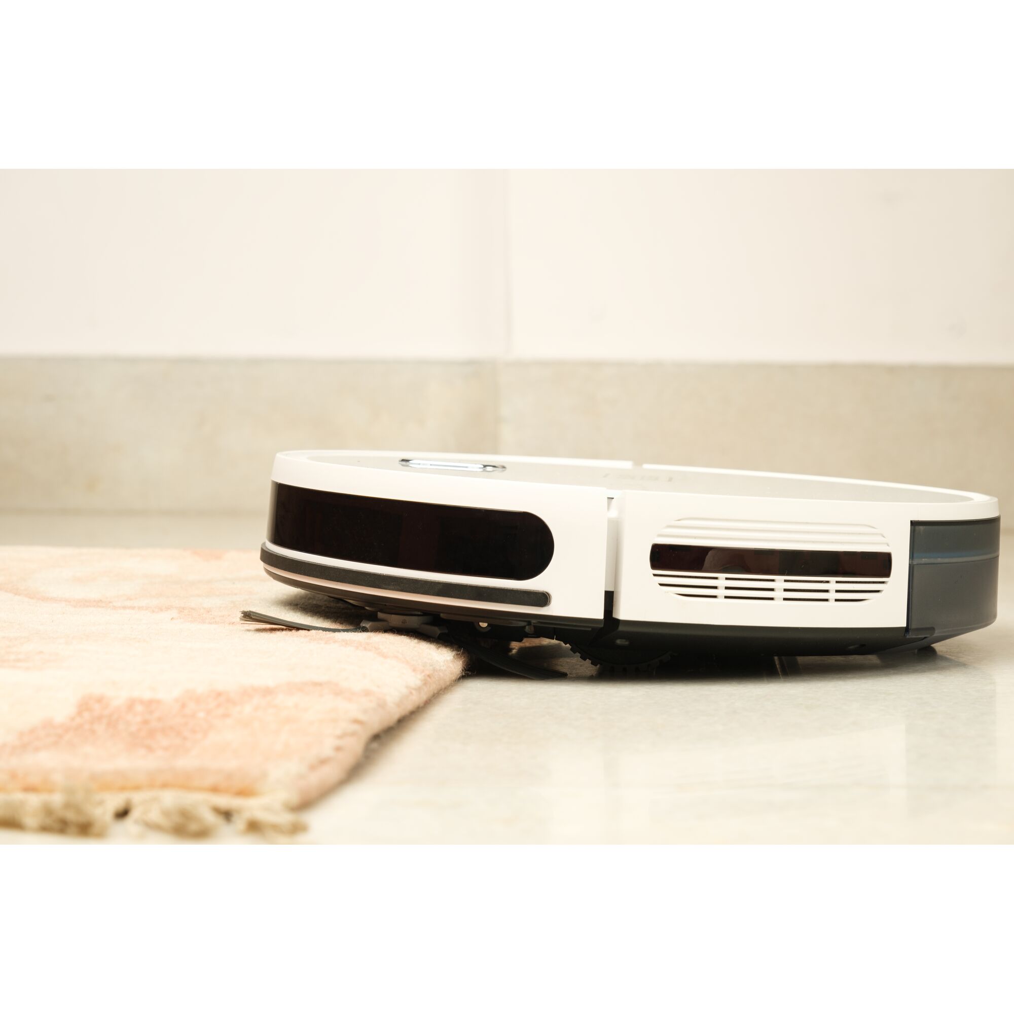 BLACKDECKER BRVA425B10 robotic vacuum cleaner in white, side view on hard floor climbing onto a rug.