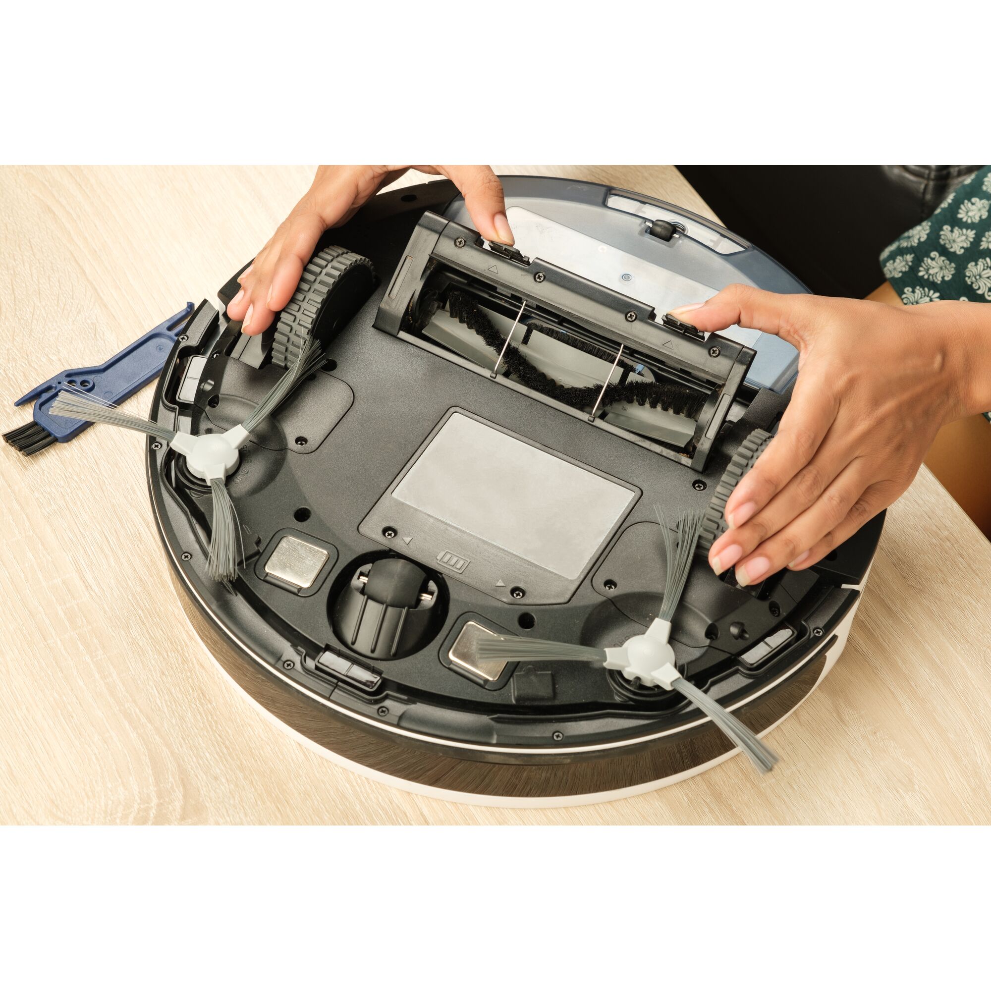 BLACKDECKER BRVA425B10 robot vacuum being maintained, showing underside with brushes and wheels.