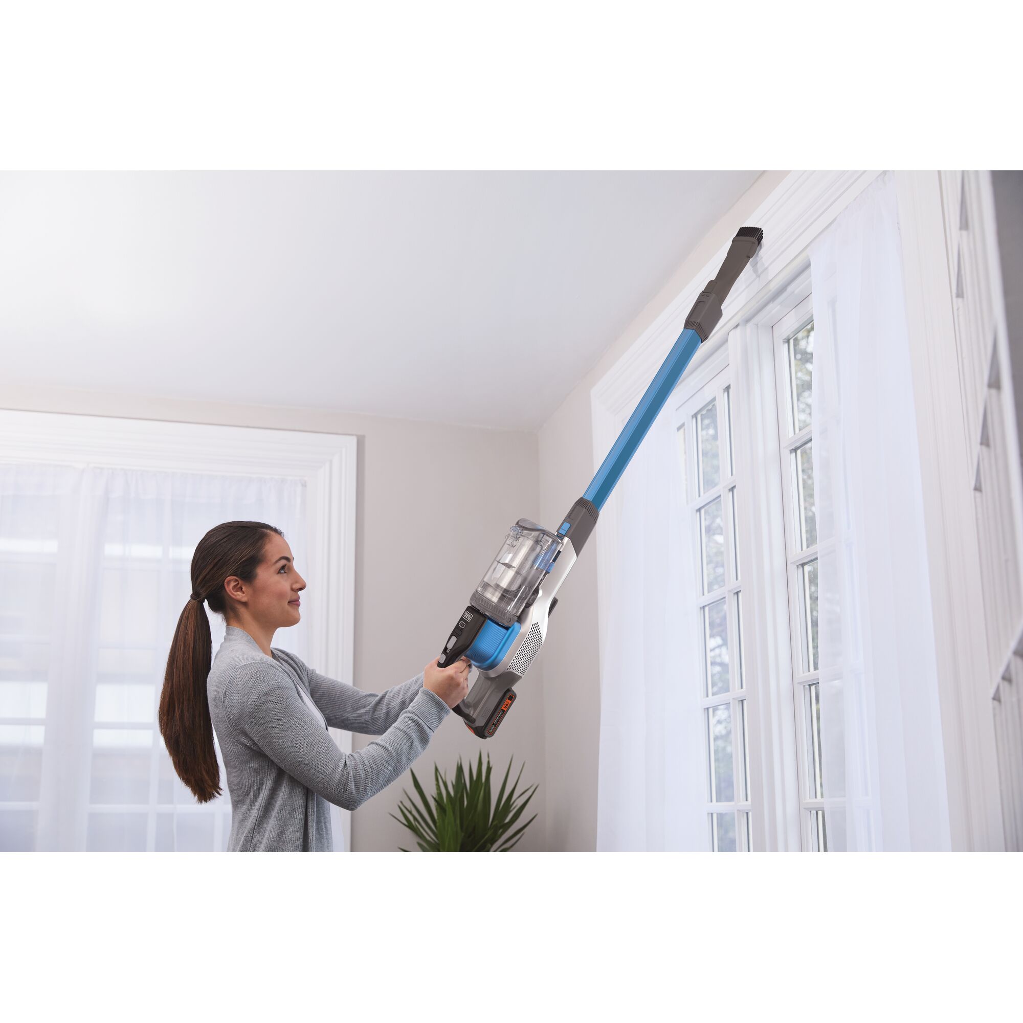 Photo of a person using BLACK+DECKER BSV2020GW cordless stick vacuum with long extension to clean window trim indoors.