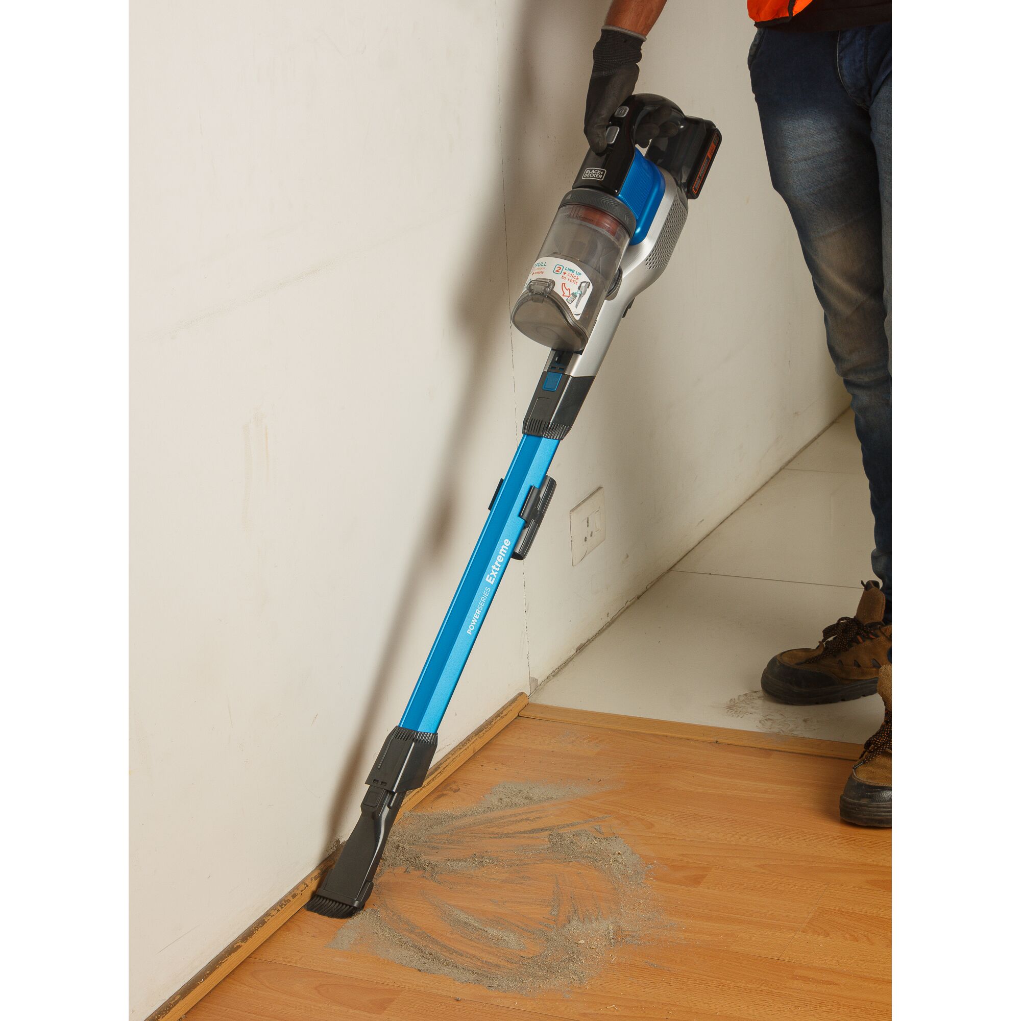 BLACKDECKER BSV2020G stick vacuum with blue body cleaning dust from floor near wall, side angle.