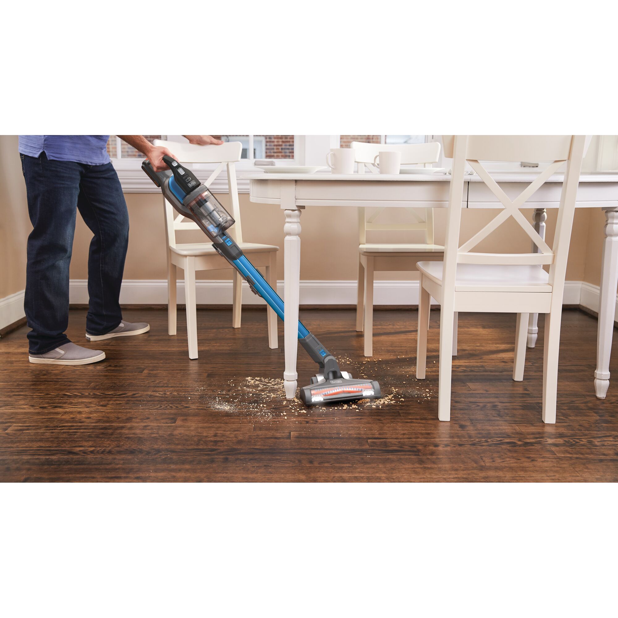 BLACKDECKER BSV2020G stick vacuum cleaning debris from hardwood floor near dining table.