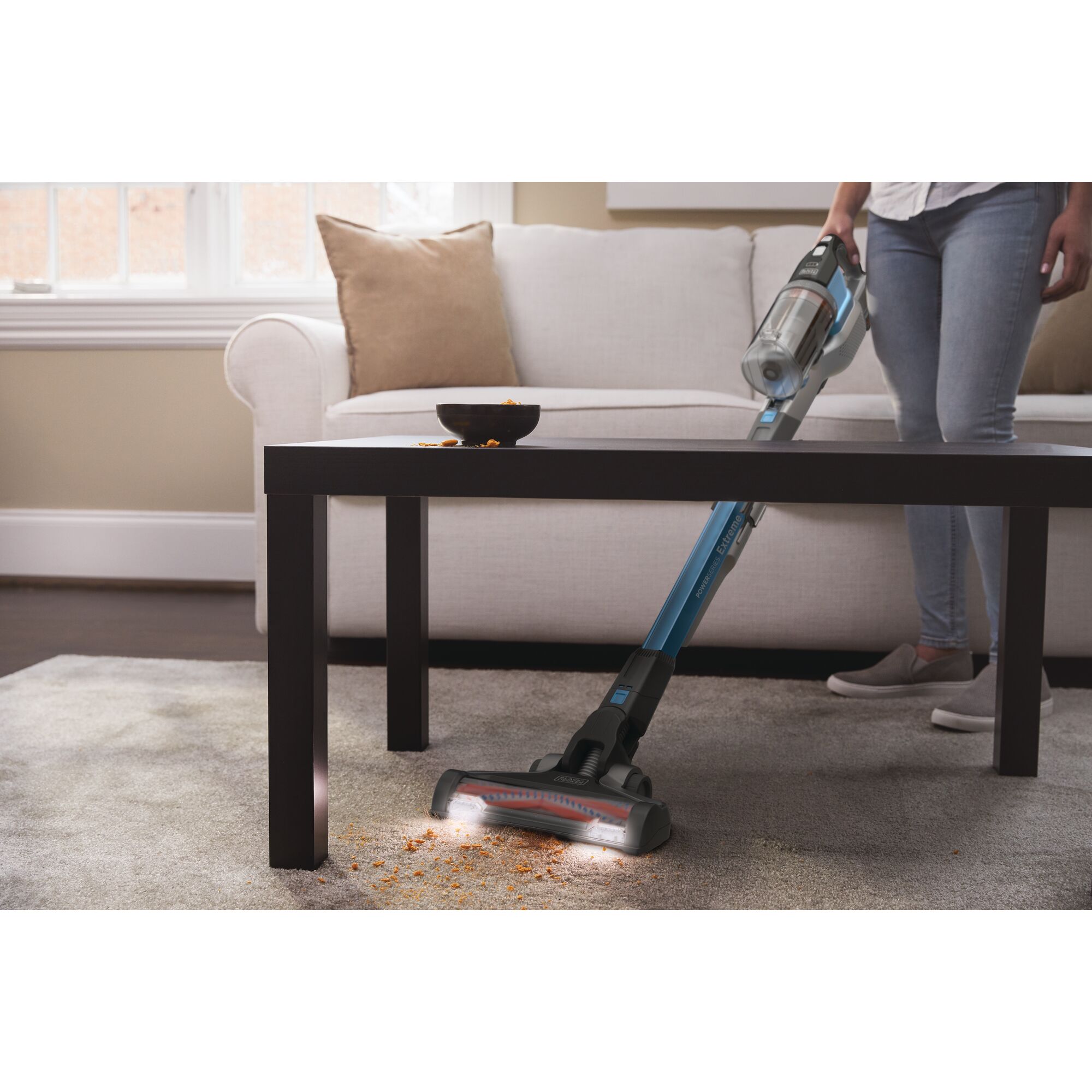 BLACKDECKER BSV2020G stick vacuum cleaning crumbs from carpet under coffee table in living room.