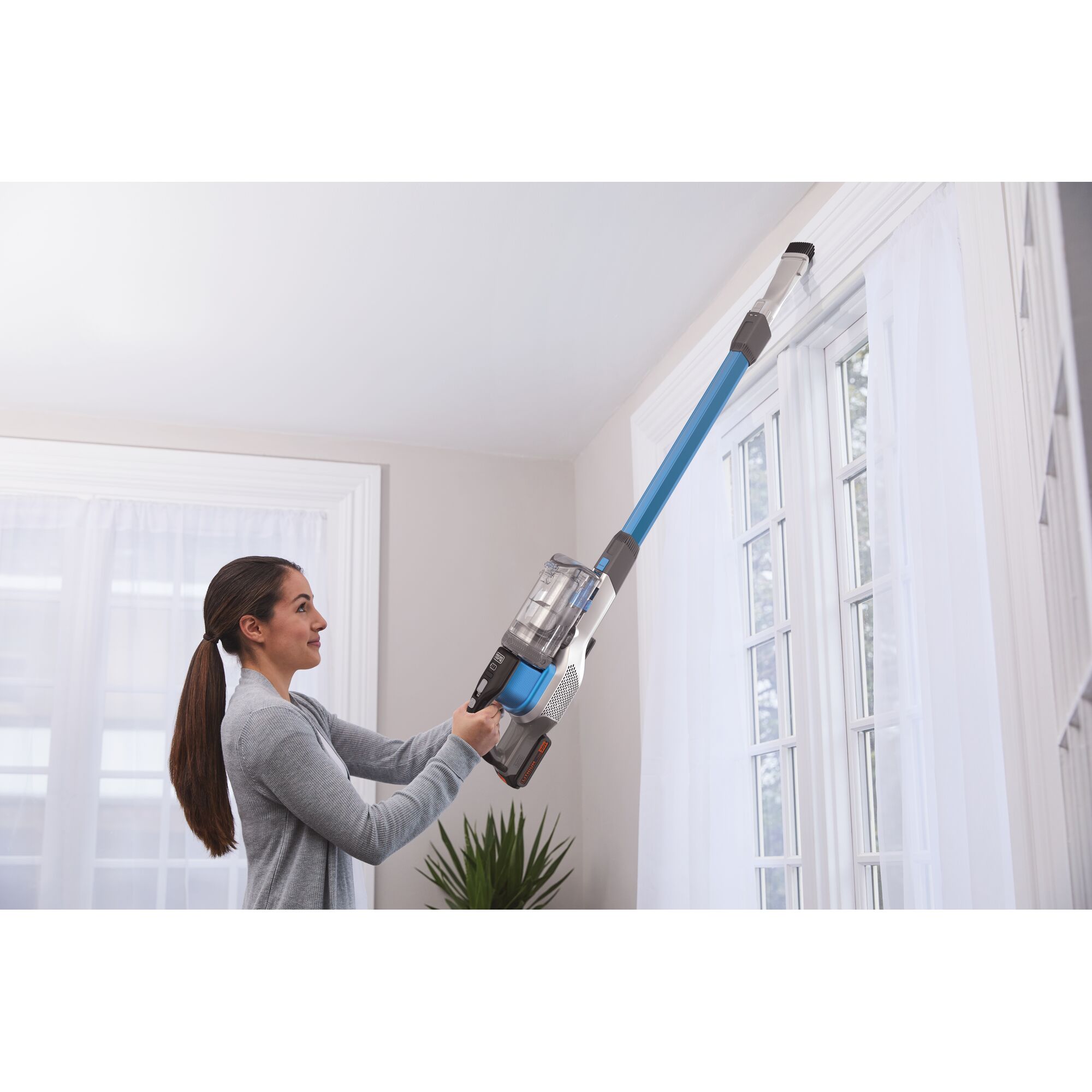 BLACKDECKER BSV2020G cordless stick vacuum with long blue extension cleaning high window trim indoors.