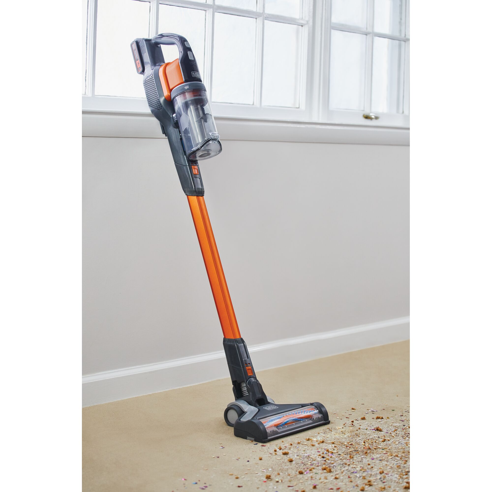 BLACKDECKER BSV2020G cordless stick vacuum, orange and black, upright on carpet with debris in front.