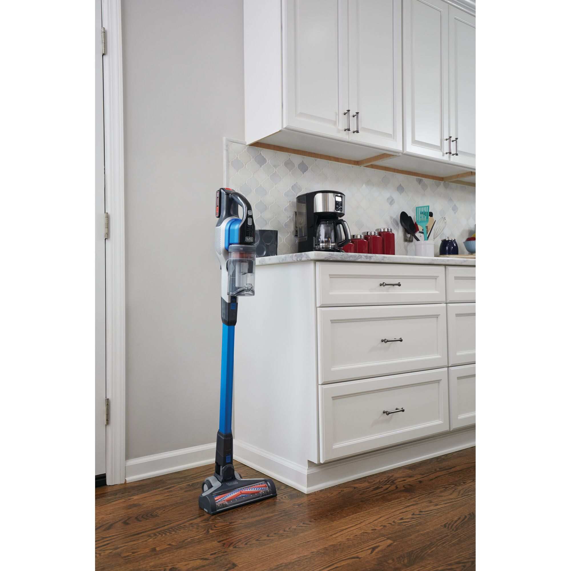 BLACKDECKER BSV2020G cordless stick vacuum cleaner with blue tube standing upright in a kitchen on hardwood floor.