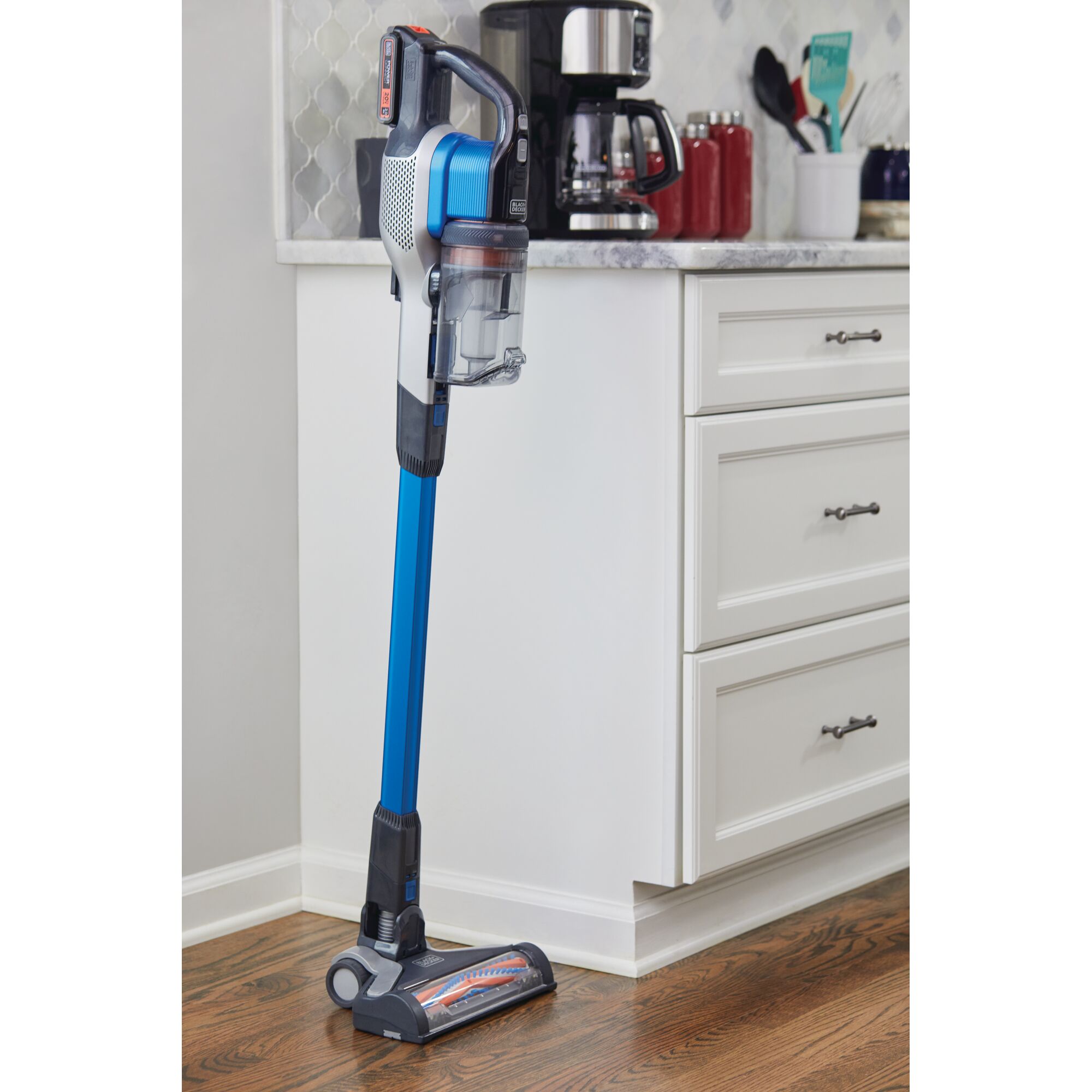 BLACKDECKER BSV2020G stick vacuum cleaner in blue and grey, upright on hardwood floor next to kitchen cabinets.