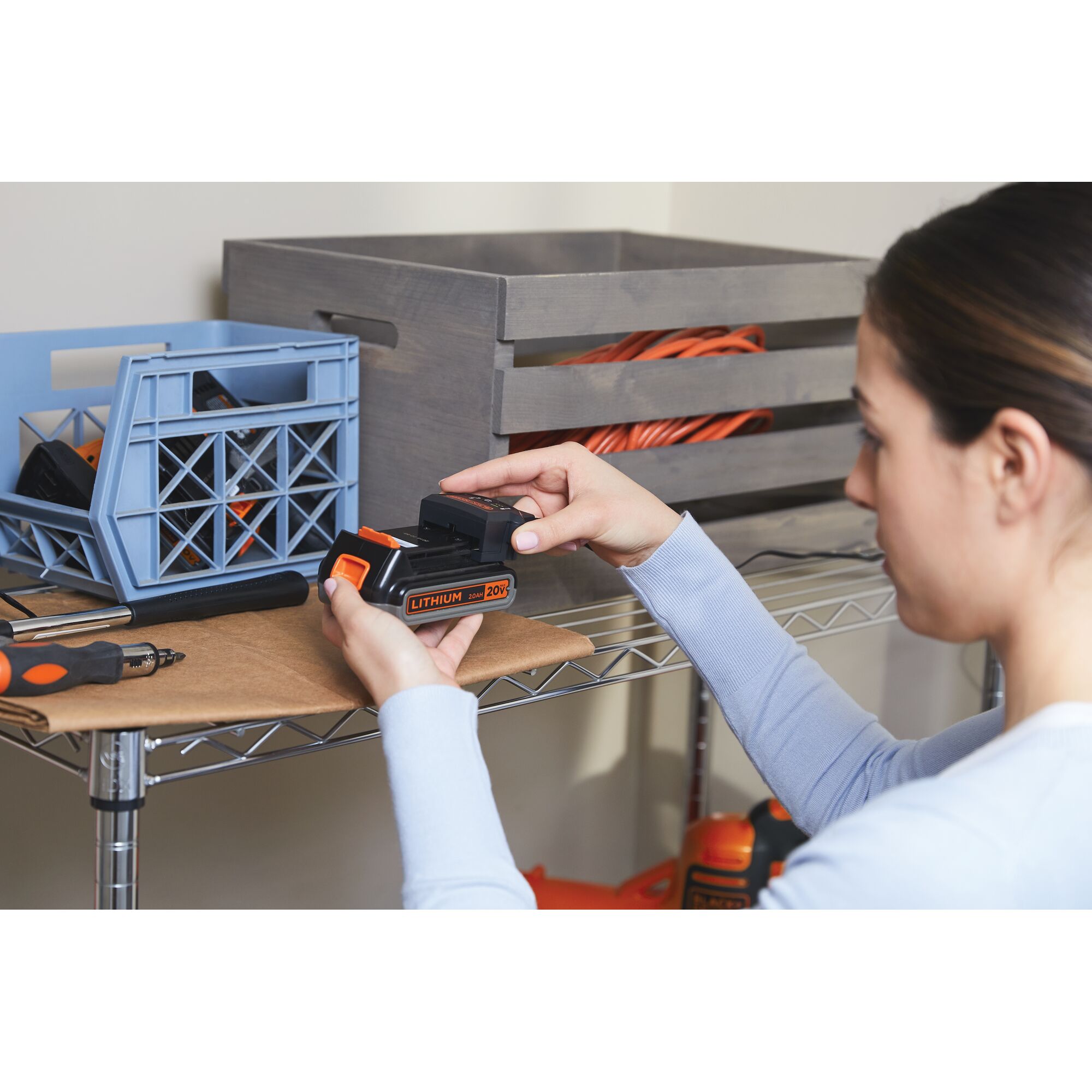 Photo of person holding BLACKDECKER 20V lithium battery BSV2020G in a workshop with tools on a wire shelf.