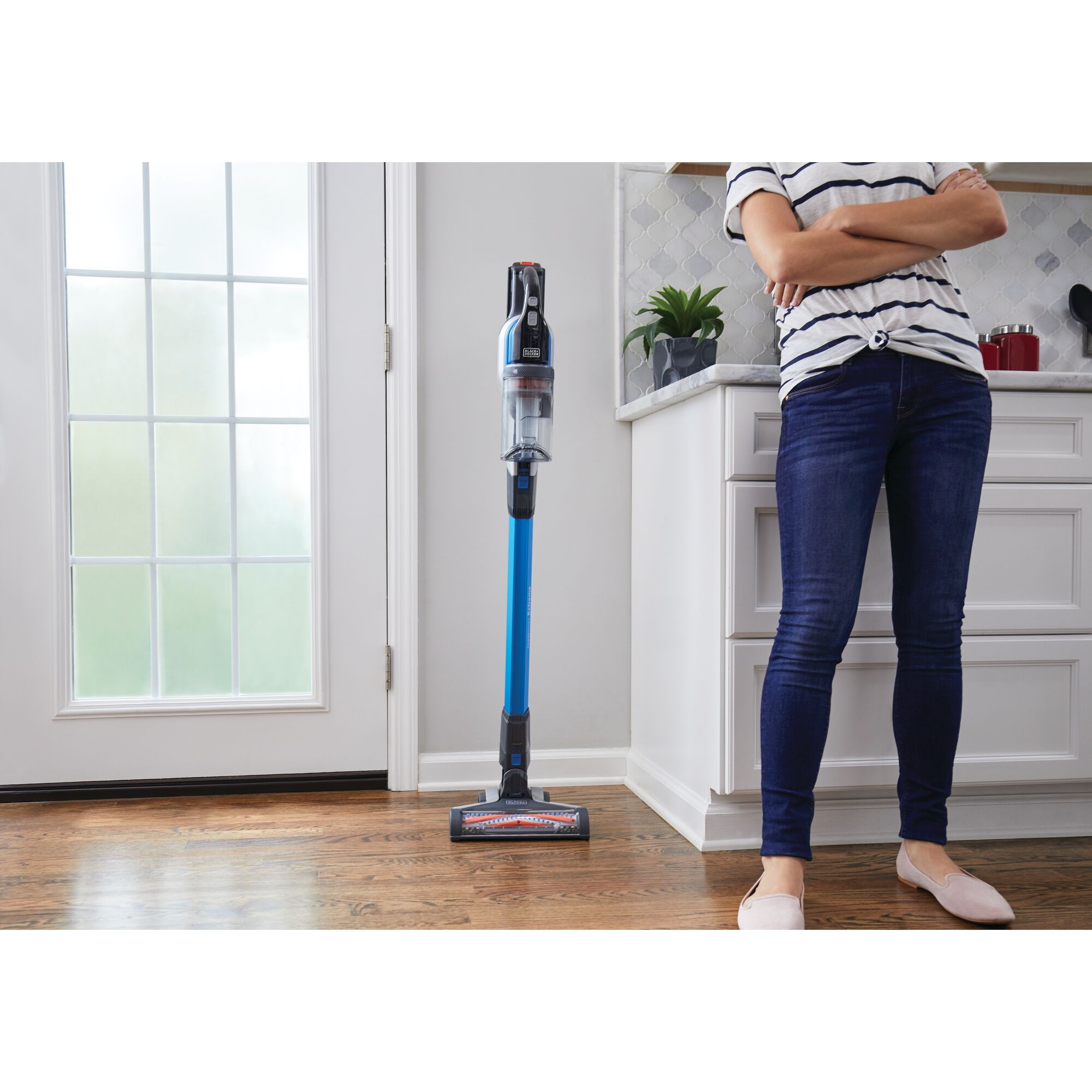 BLACKDECKER BSV2020G stick vacuum with blue tube standing upright on hardwood floor in a kitchen next to a person.