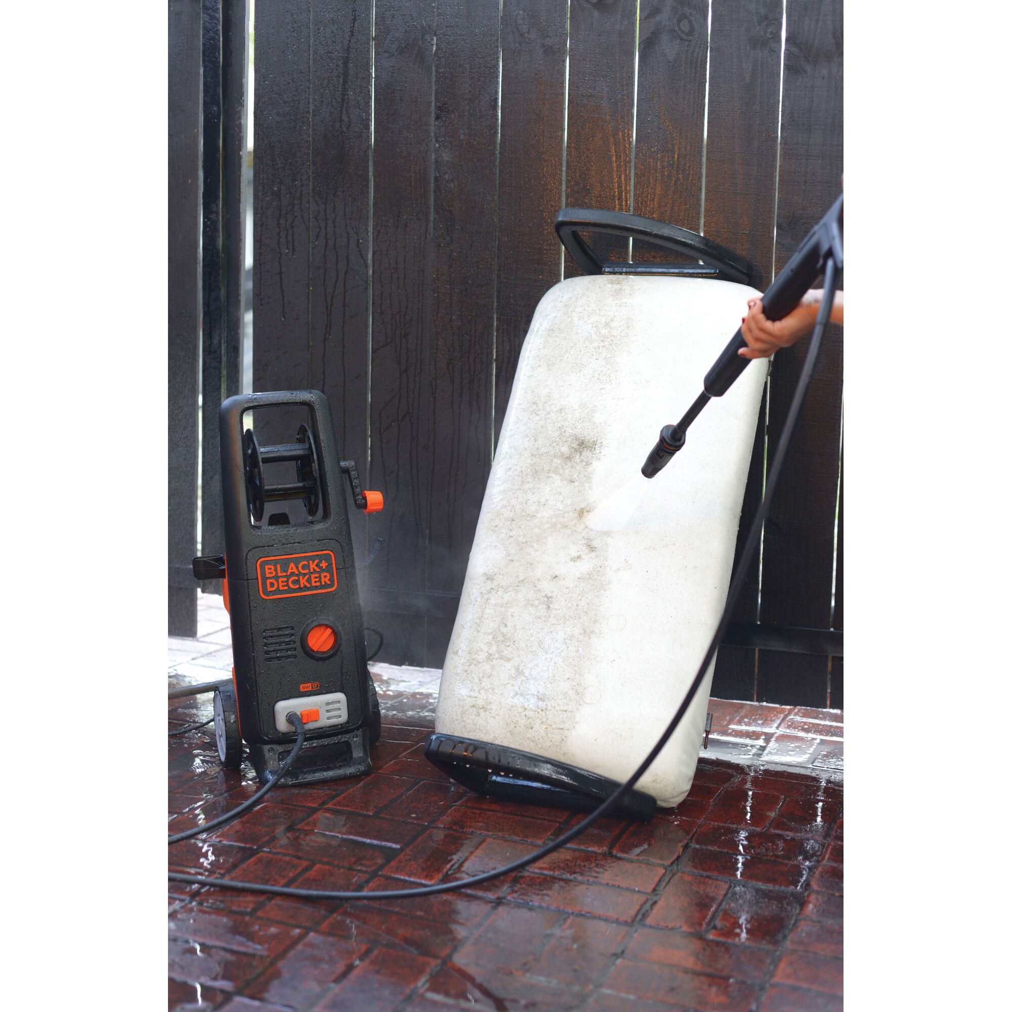 BLACKDECKER BW17 pressure washer cleaning a dirty outdoor cushion on wet brick patio.