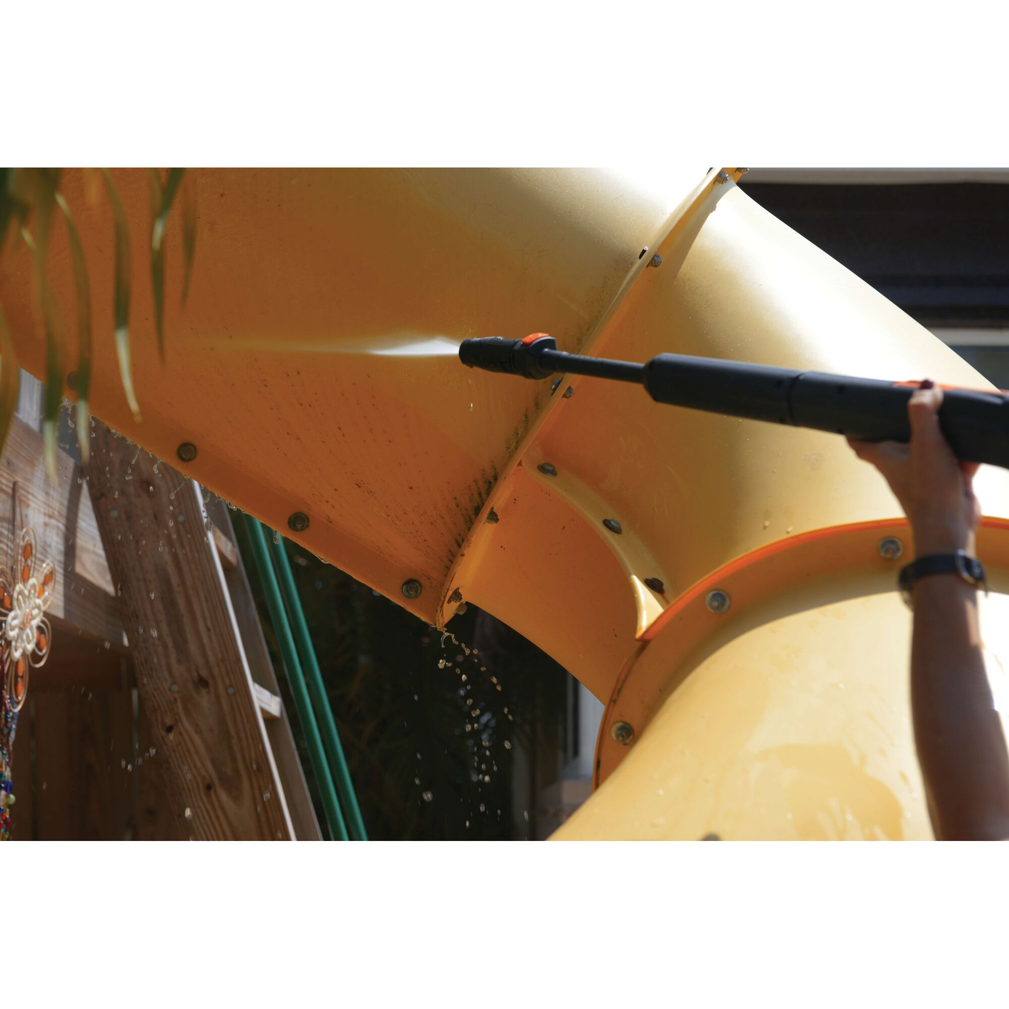 BLACKDECKER BW17 pressure washer spraying yellow outdoor slide, cleaning dirt, side angle.
