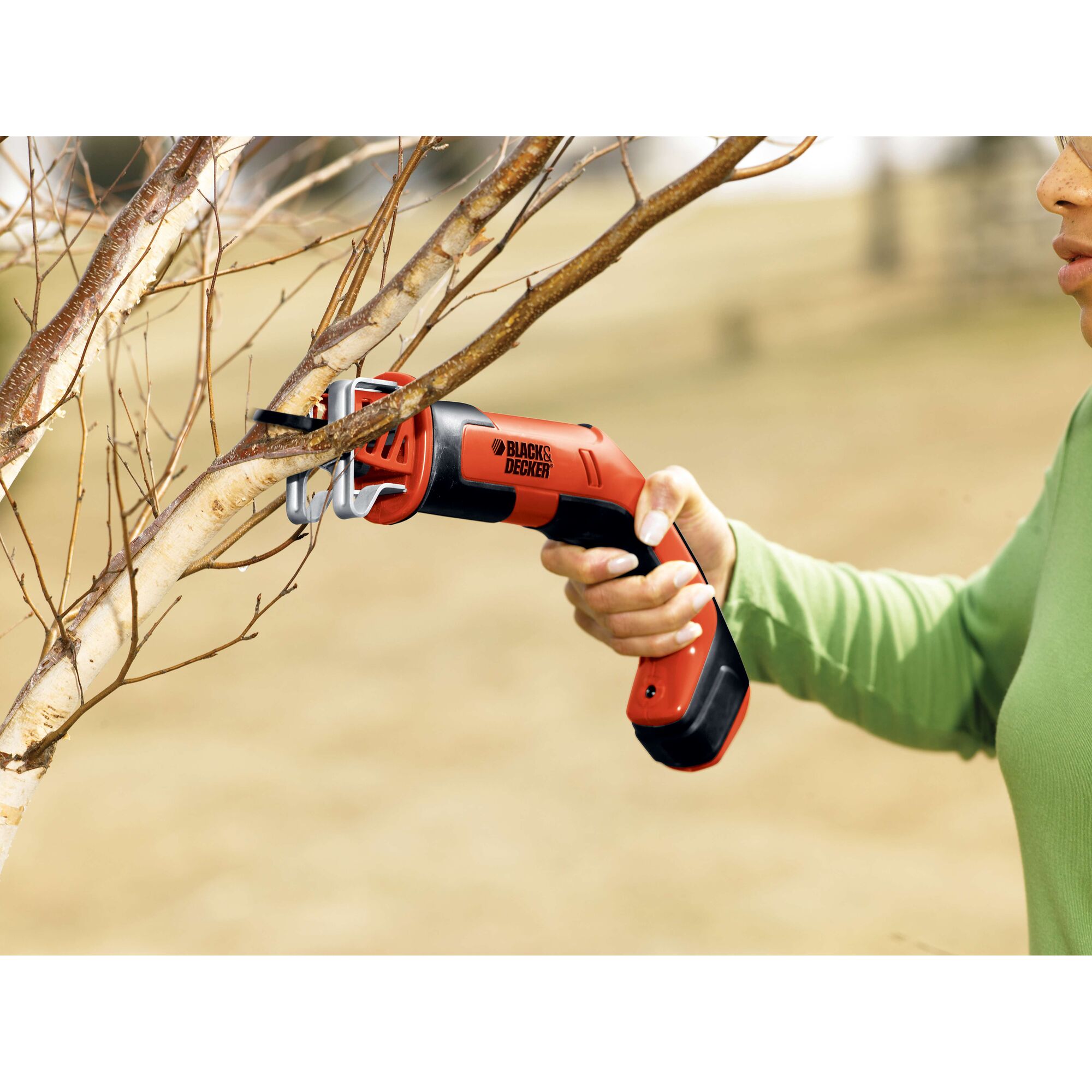BLACK+DECKER CHS6000 cordless pruning saw cutting a tree branch outdoors.