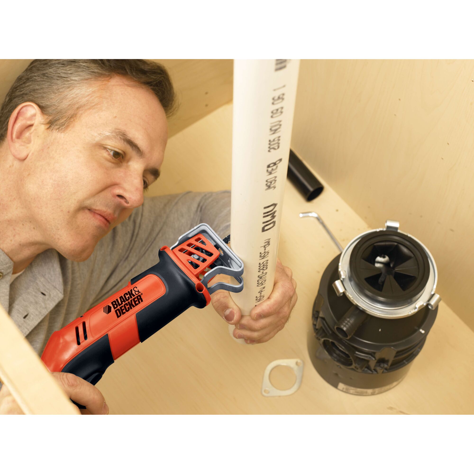 BLACKDECKER CHS6000 reciprocating saw used to cut a white PVC pipe under a sink, close-up view.