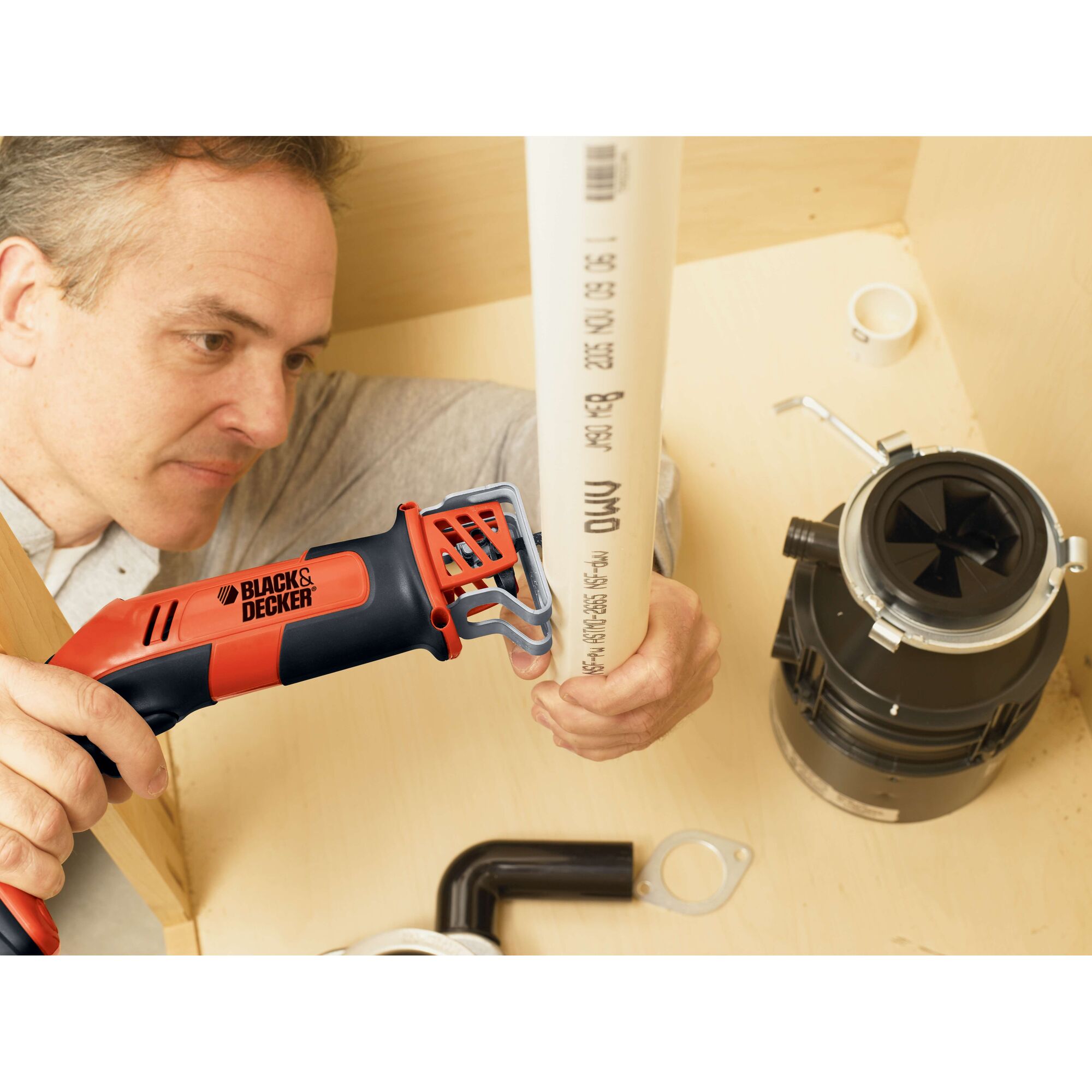 BLACK+DECKER CHS6000 reciprocating saw cutting white PVC pipe in plumbing installation scene.
