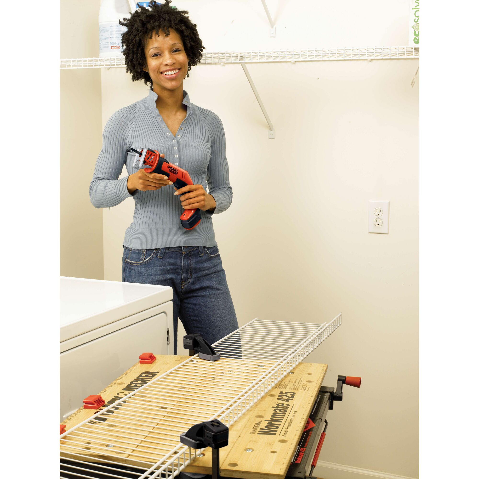 Photo of a person holding a BLACKDECKER CHS6000 cordless power tool, standing in a laundry room beside a workbench and wire shelf.