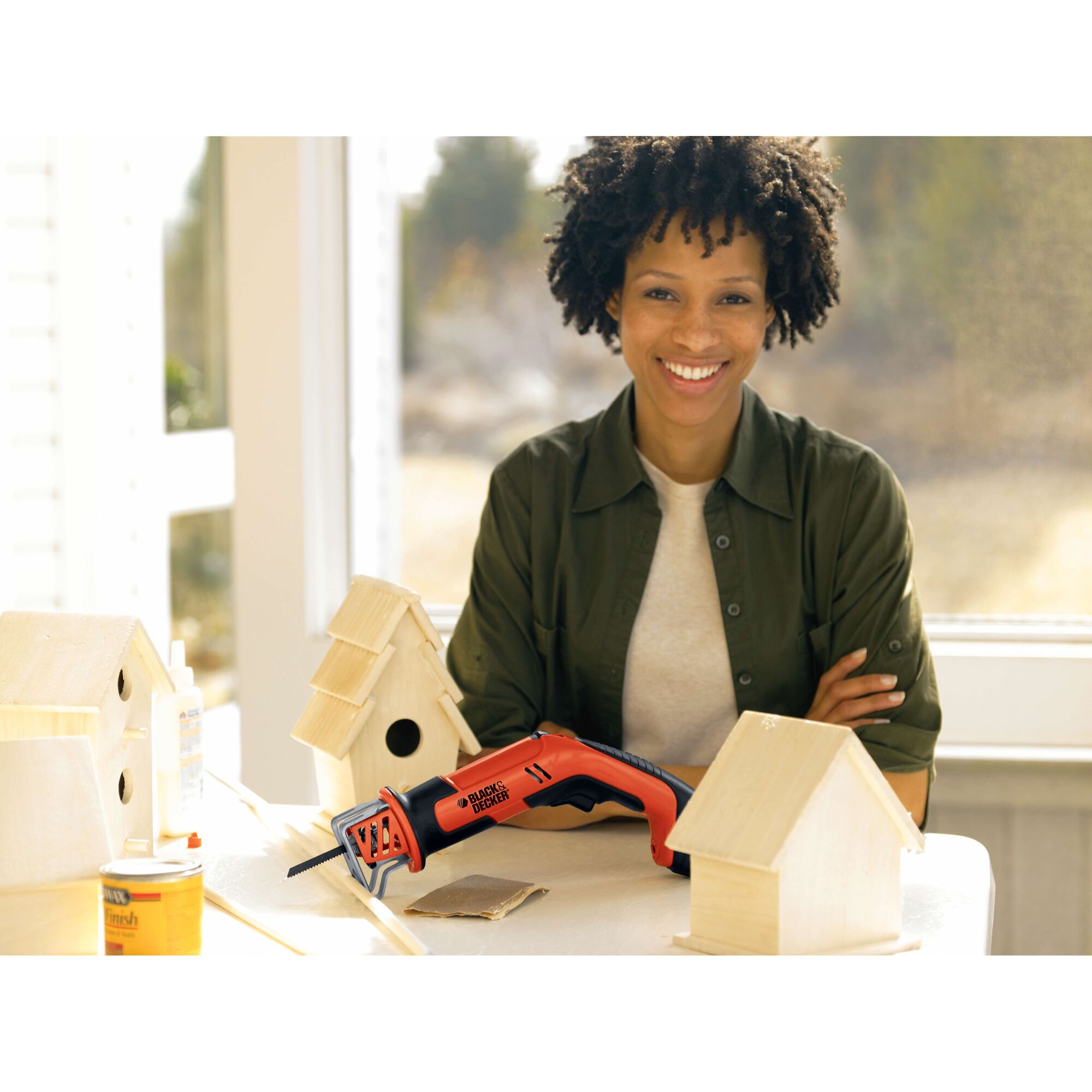 BLACK+DECKER CHS6000 cordless saw on table near unfinished birdhouses in bright indoor workshop.