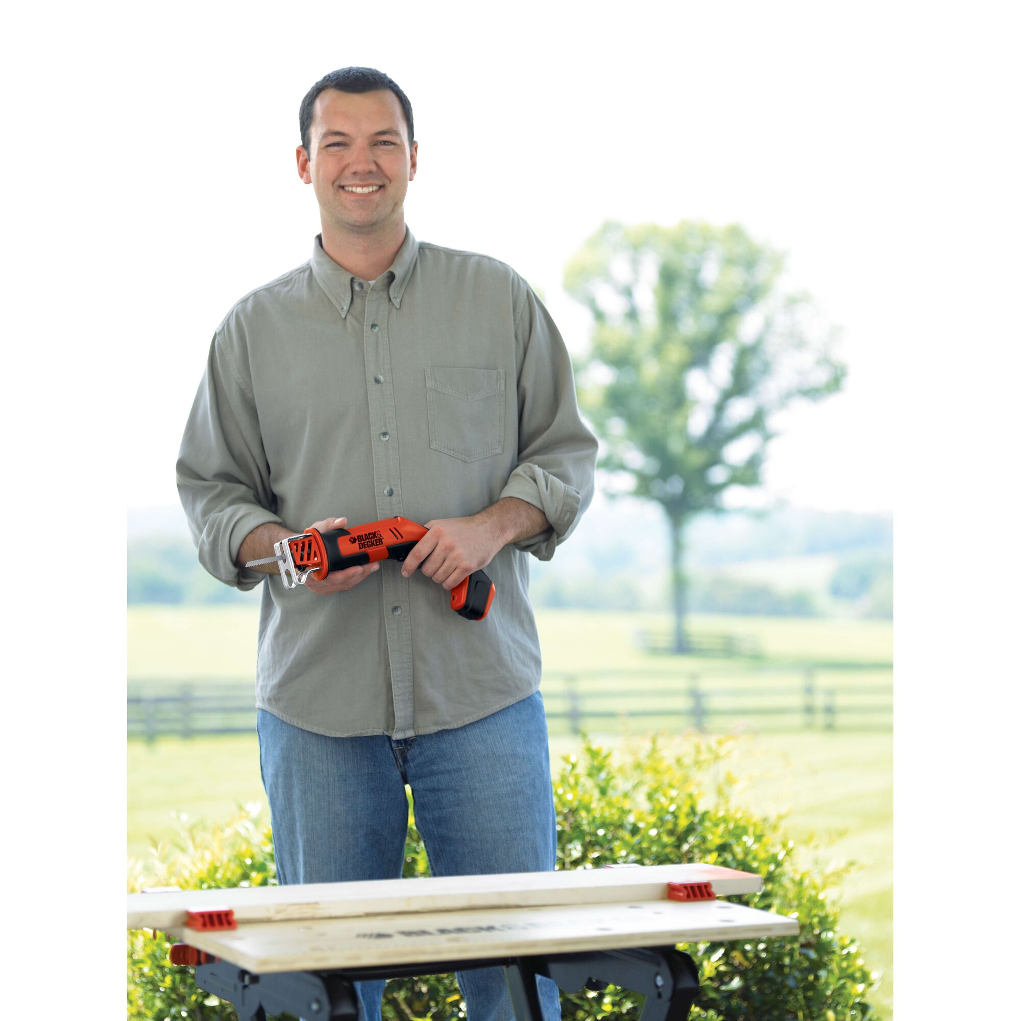 Person holding BLACK+DECKER CHS6000 cordless saw in outdoor setting, standing behind a workbench.