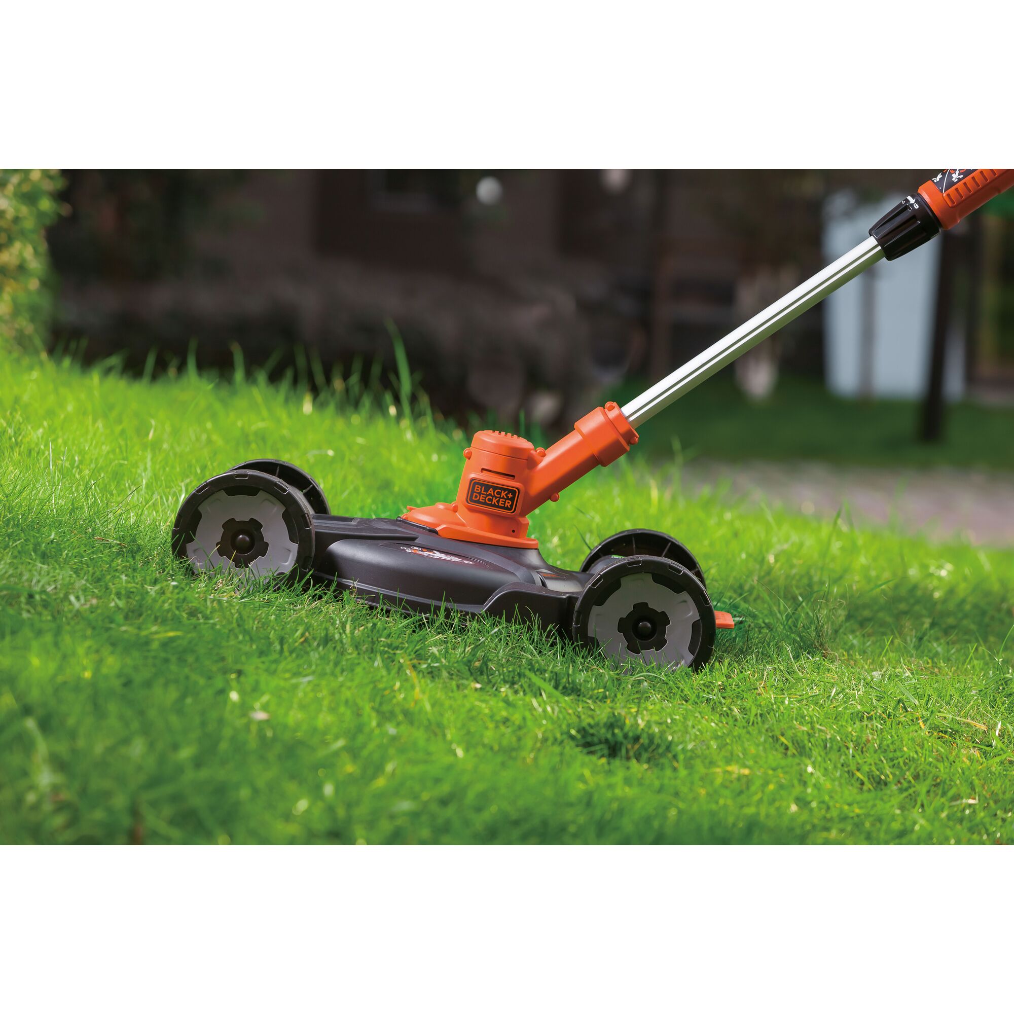 BLACKDECKER CM100N lawn mower attachment with orange and black body, shown in use on green grass.