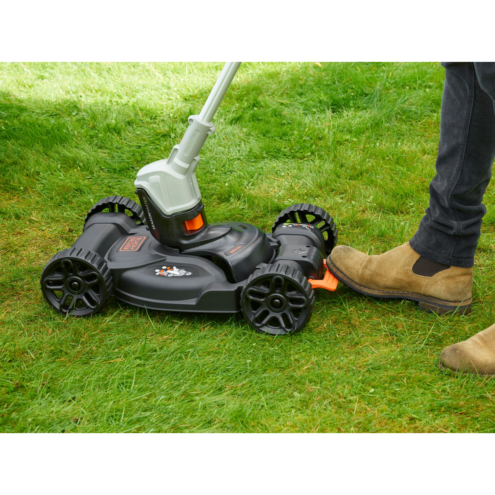 BLACKDECKER CM100 lawn mower attachment on grass, side view, black and orange design with foot pedal.