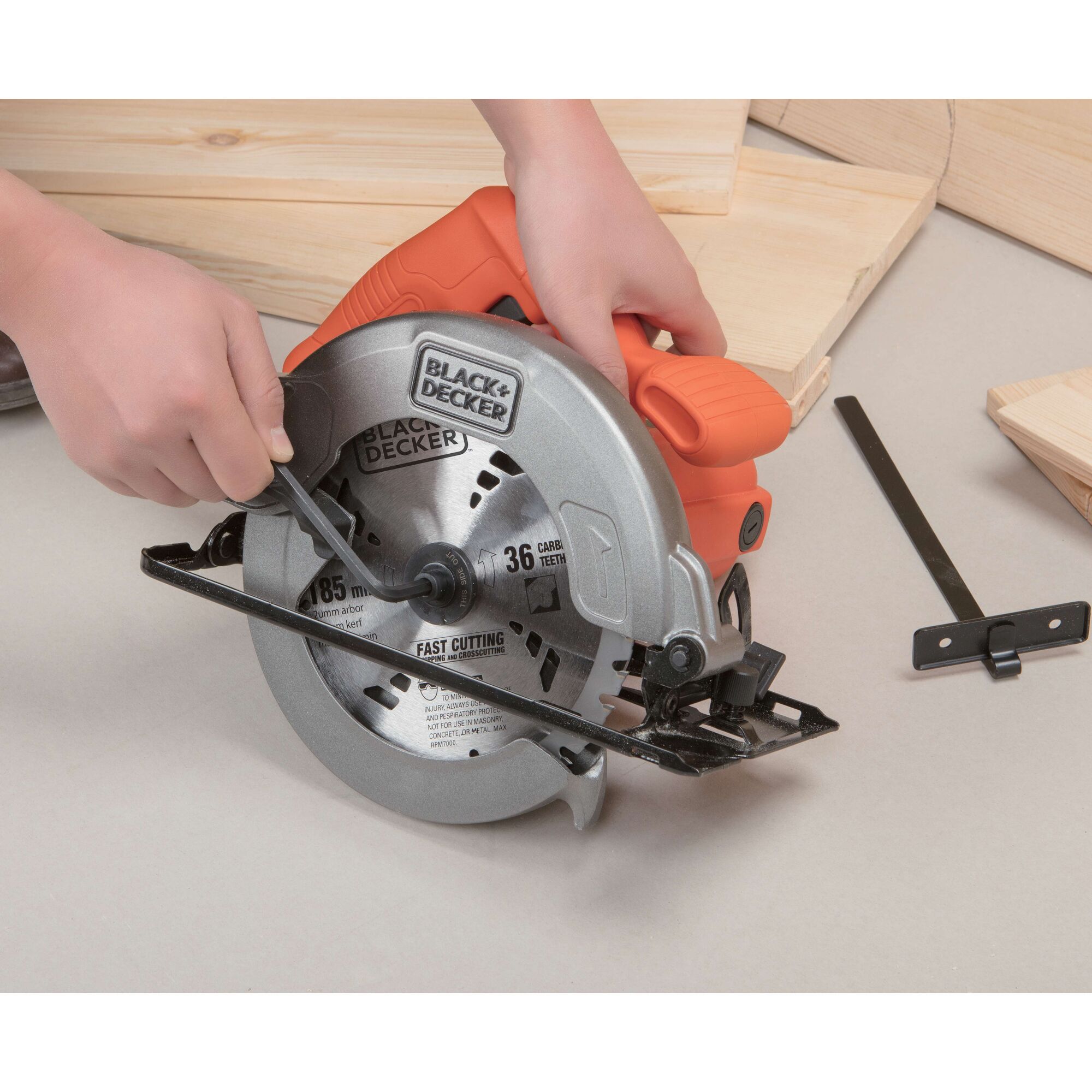 BLACKDECKER CS1004 circular saw with orange handle, photographed from side angle, hands adjusting blade.