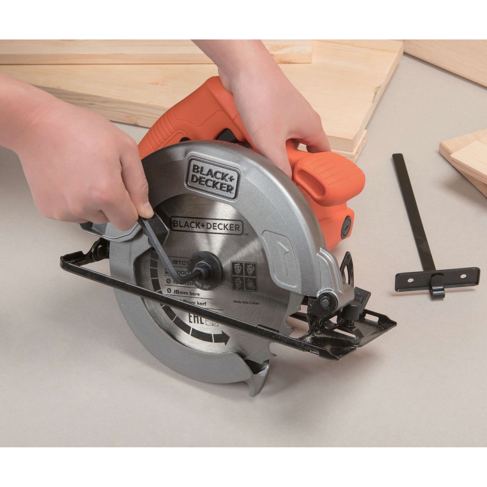 BLACK+DECKER CS1004 circular saw with orange handle, close-up being adjusted, surrounded by wood pieces.