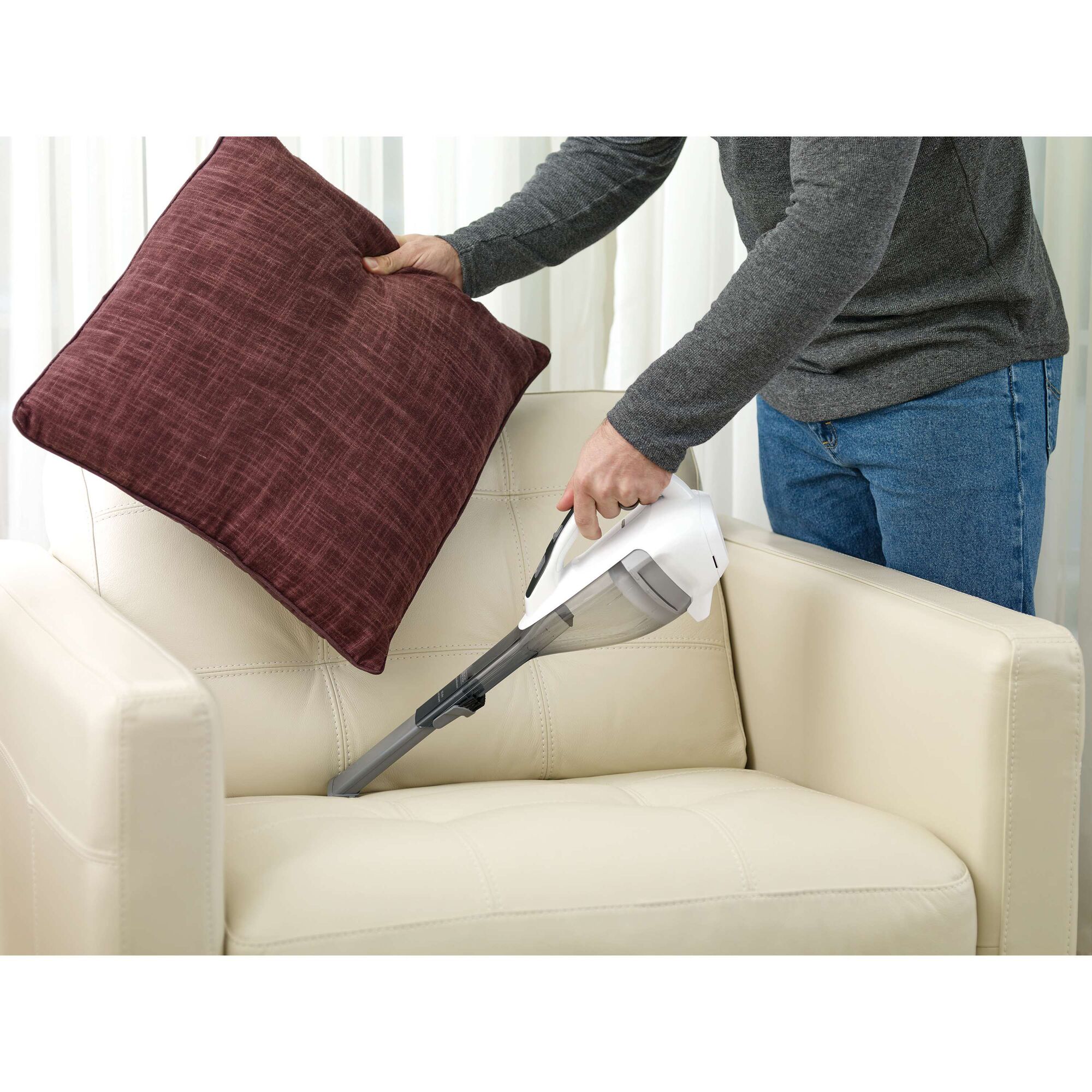 BLACKDECKER DVA315JF handheld vacuum cleaning beige sofa under maroon pillow indoors.