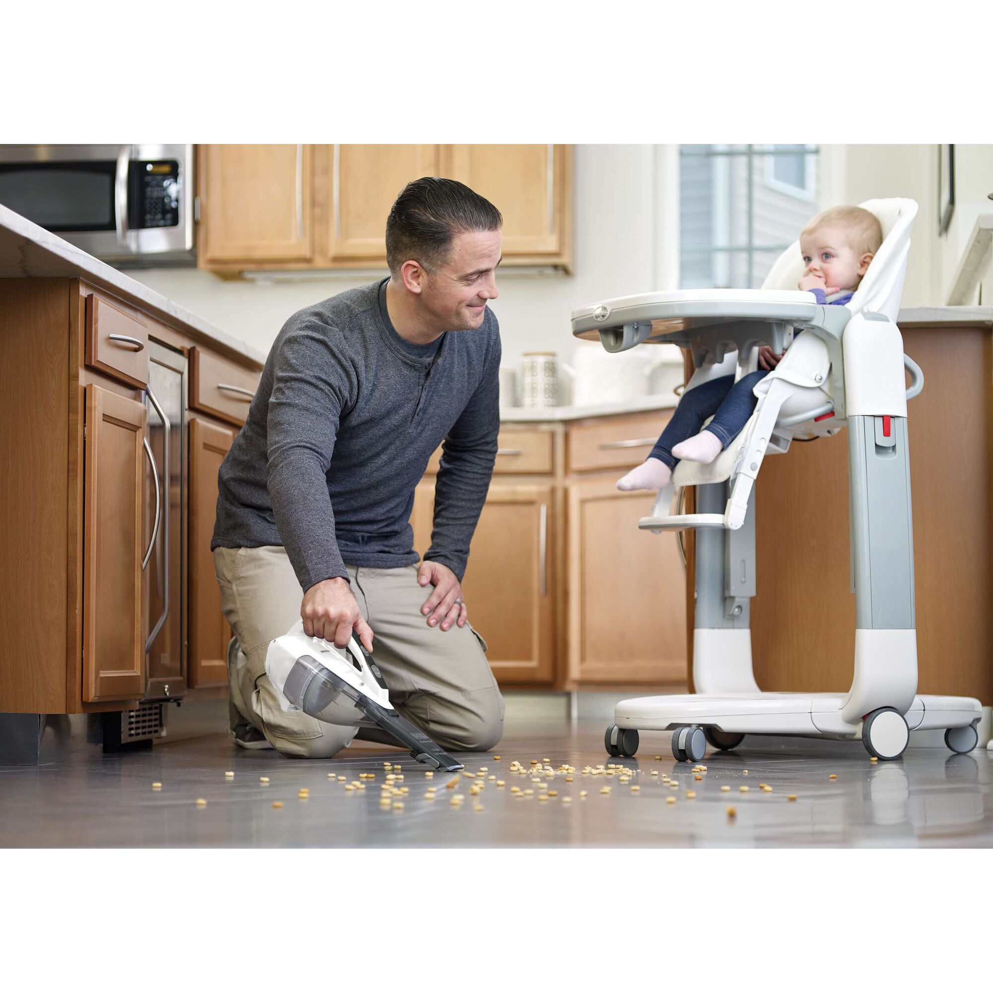 BLACKDECKER DVA315J handheld vacuum cleaning spilled food near a high chair in kitchen setting.