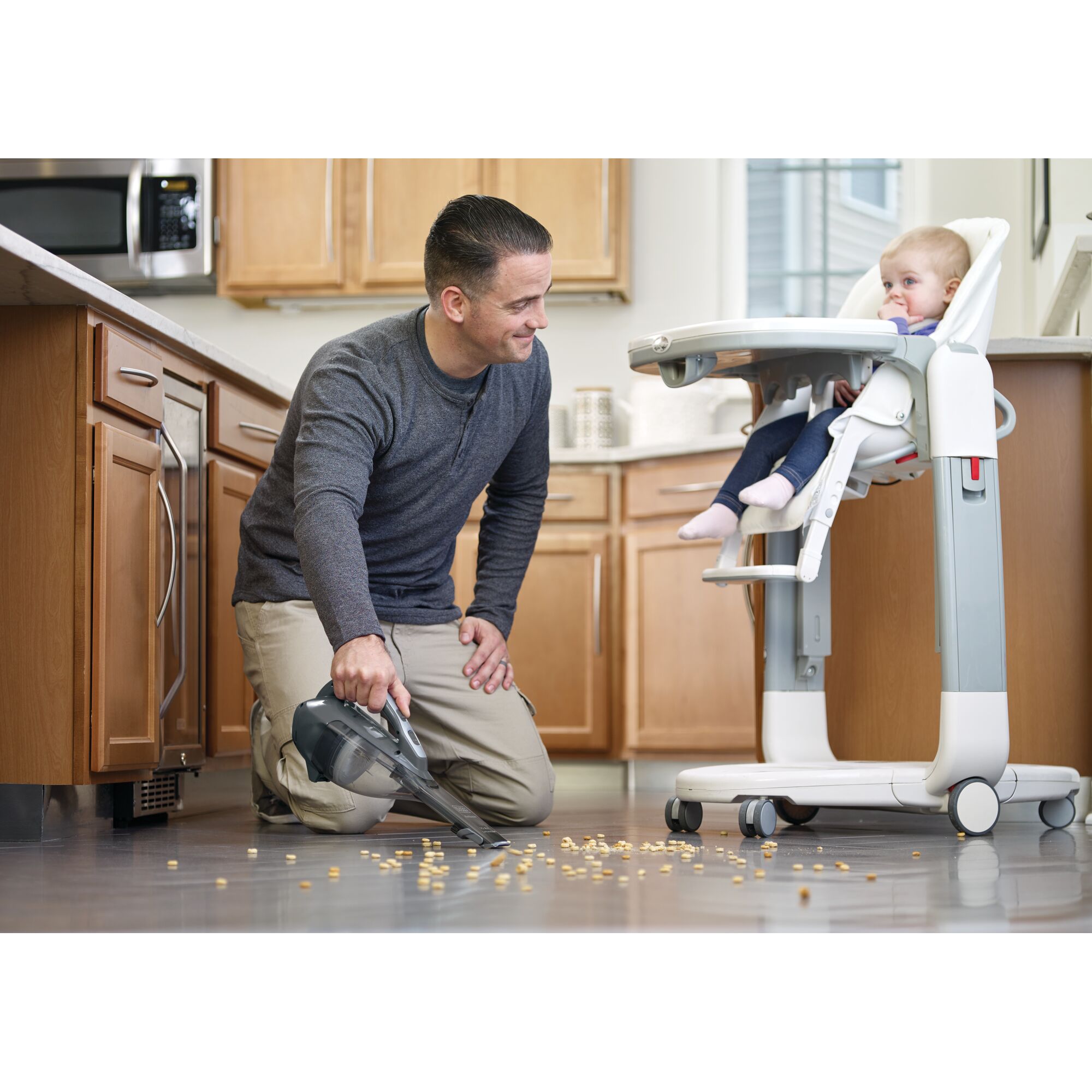 BLACK+DECKER DVA320BF handheld vacuum cleaning cereal from kitchen floor near high chair.