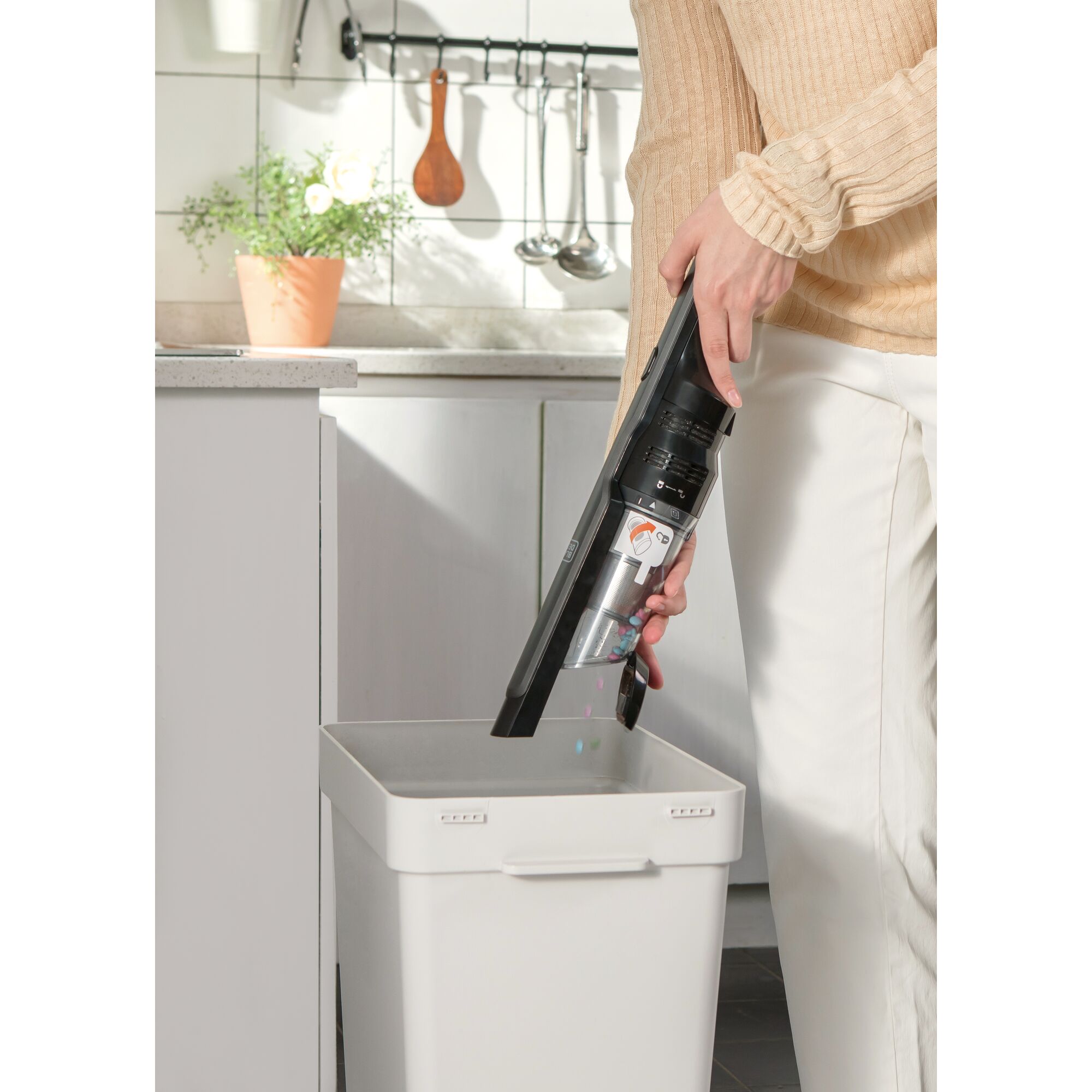 BLACKDECKER DVC320B01 handheld vacuum being emptied into a bin in a kitchen setting.